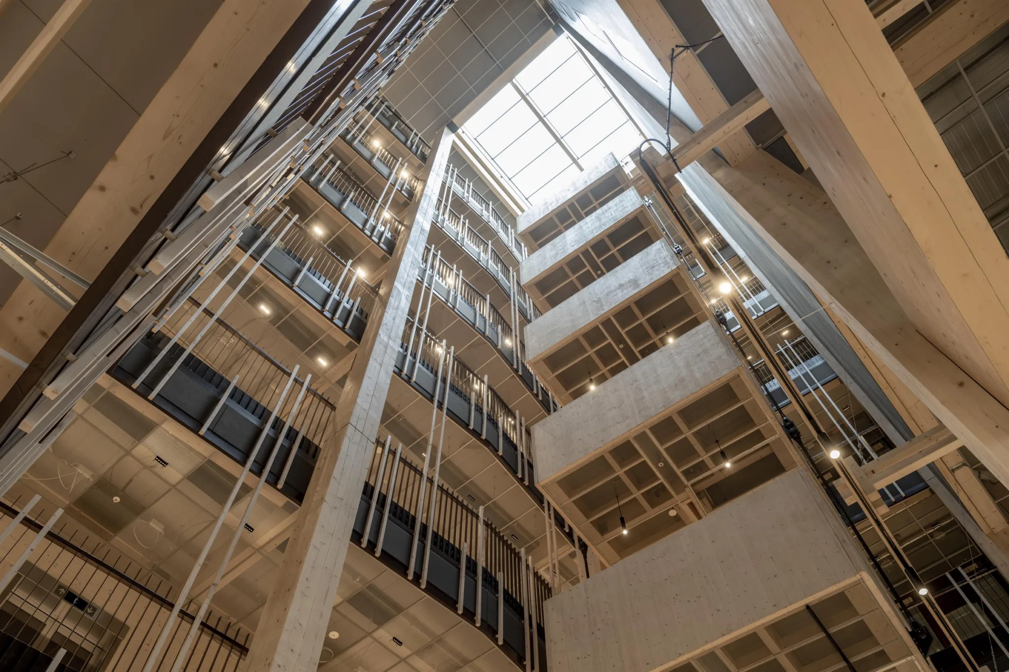 1. Interiör av en modern byggnad med flera våningar, sett från bottenvåningen upp mot ett takfönster med naturligt ljus.