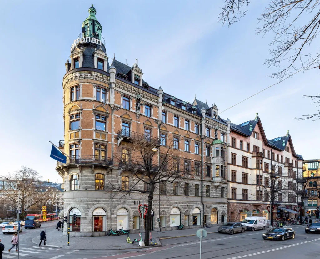 En hörnbyggnad med orange fasad och ett torn, prydd med flaggor och omgiven av stadsgata.