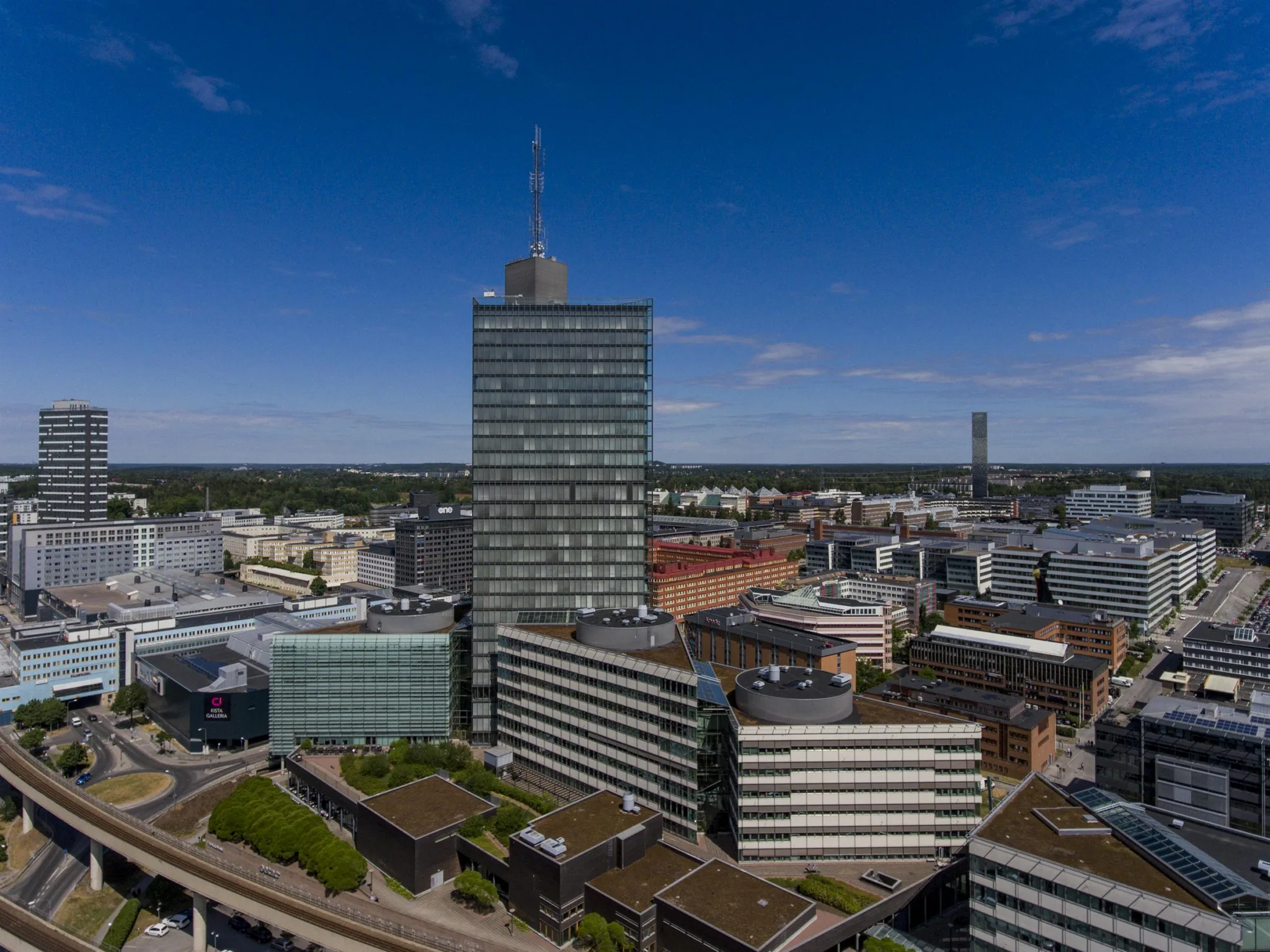 5. En stadsvy med en hög byggnad i centrum, omgiven av lägre kontorsbyggnader och en klar blå himmel.