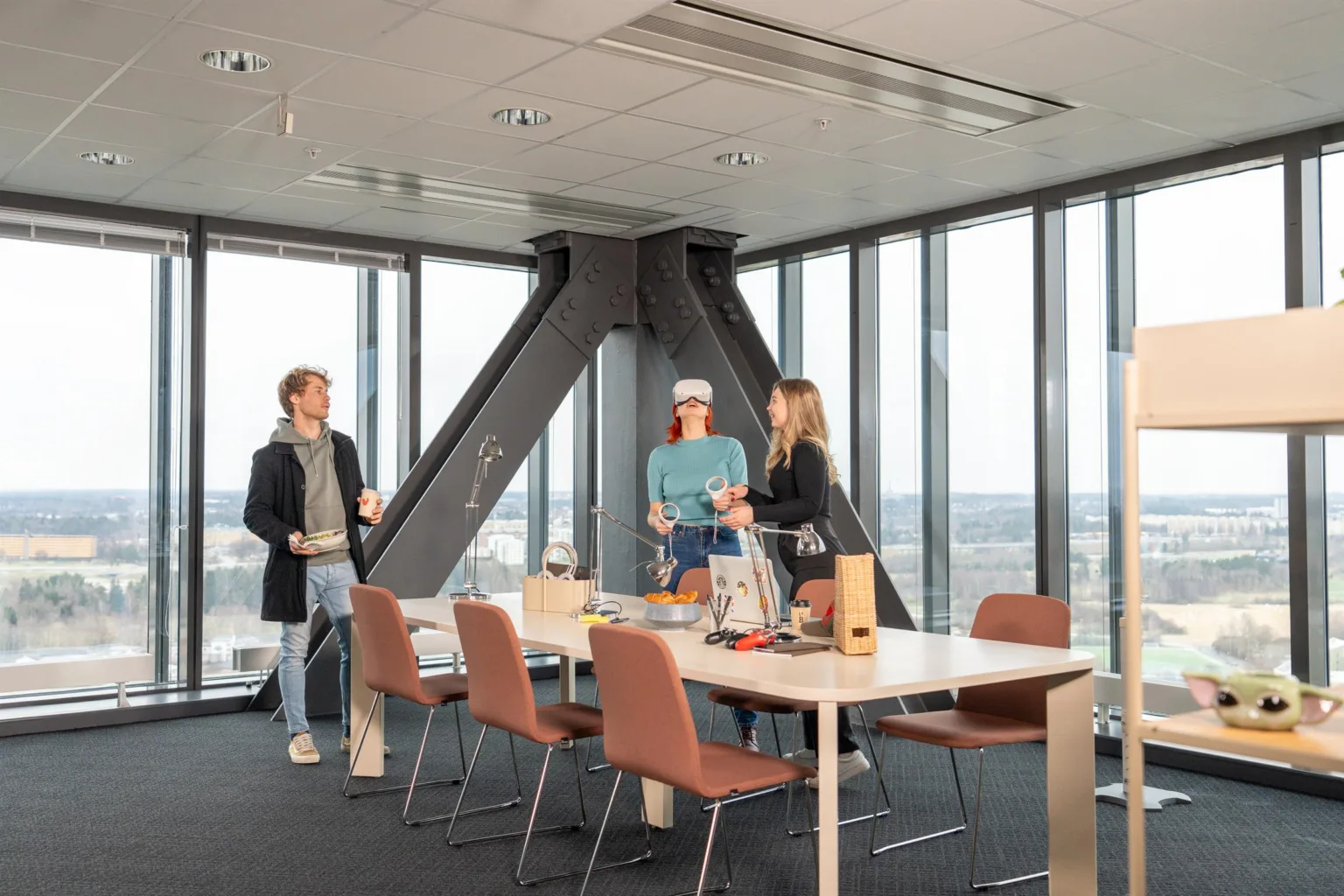 1. Tre personer står vid ett bord i ett modernt konferensrum med stora fönster och utsikt över staden.