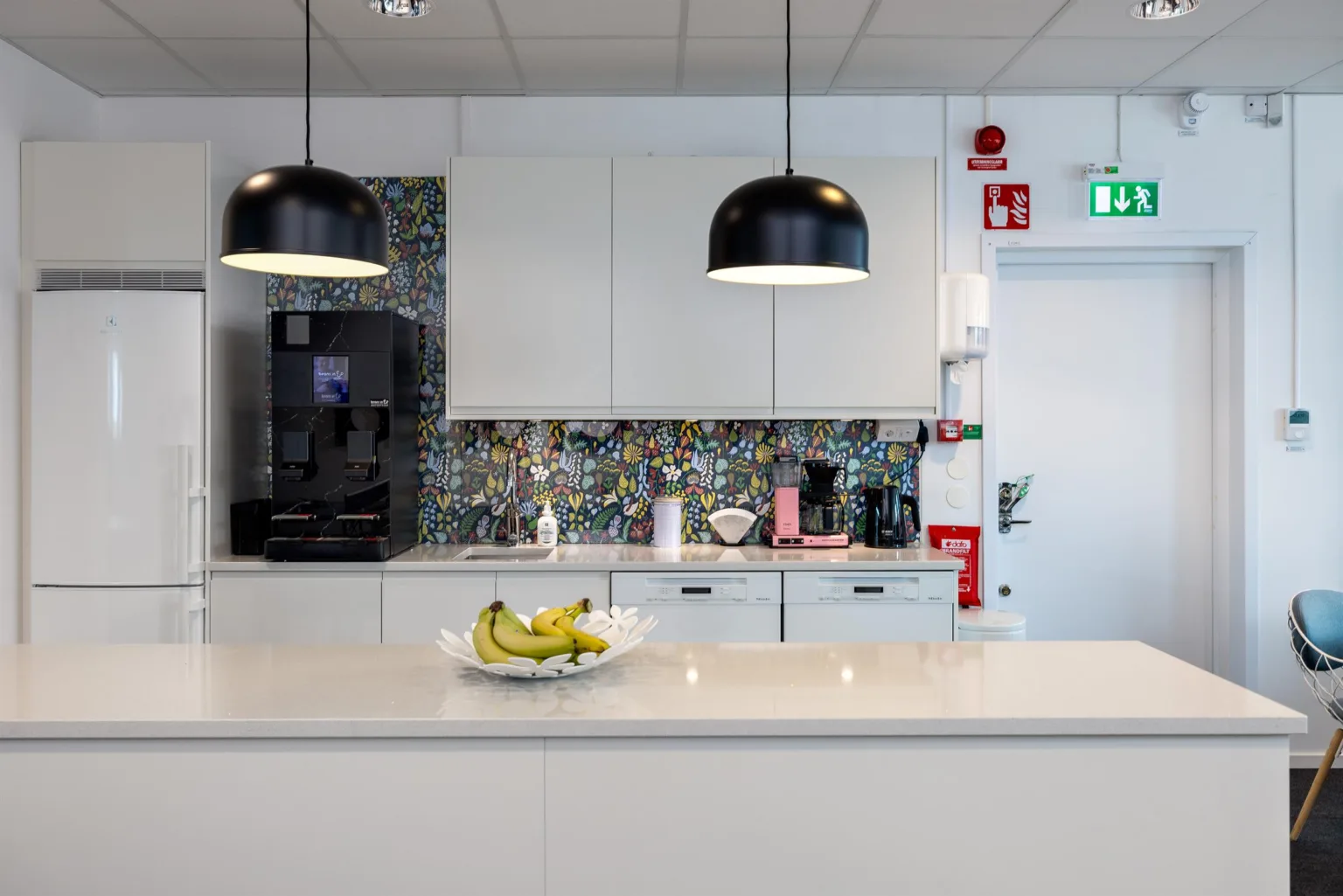 2. Ett modernt kök med en köksö, hängande lampor och en fruktskål med bananer.