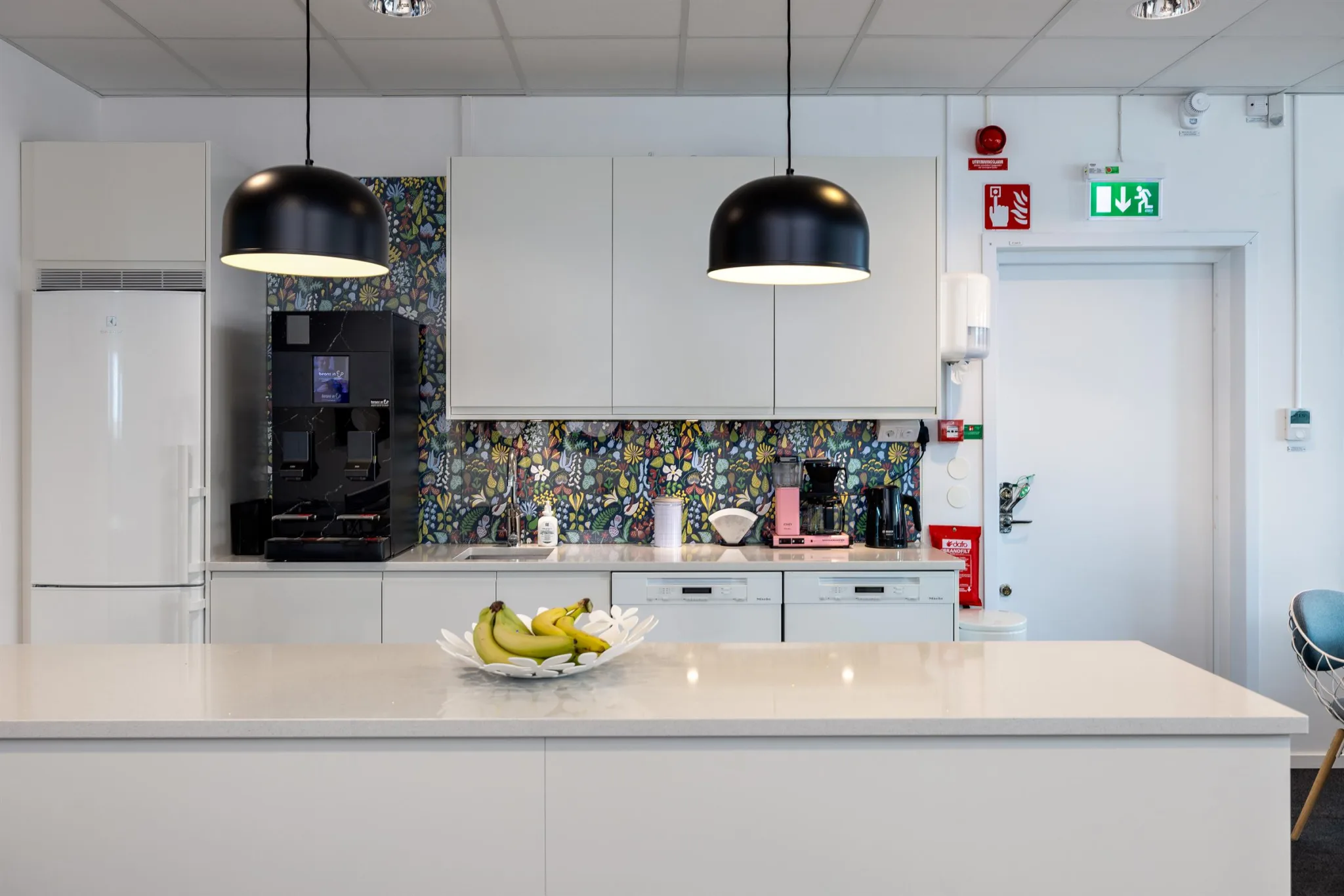 2. Ett modernt kök med en köksö, hängande lampor och en fruktskål med bananer.