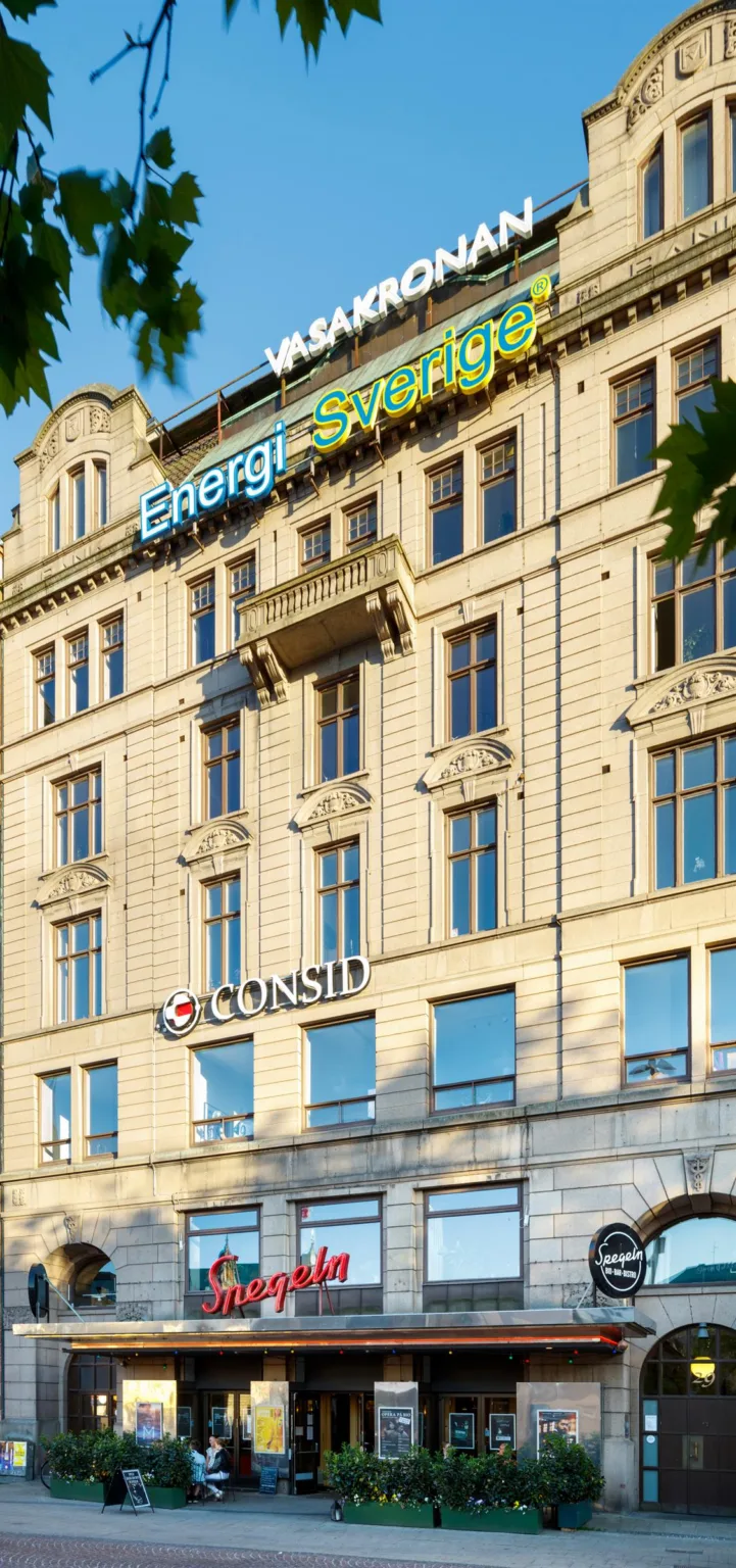 Fasad av en ljus byggnad med skyltar som visar "Energi" och "Consid".