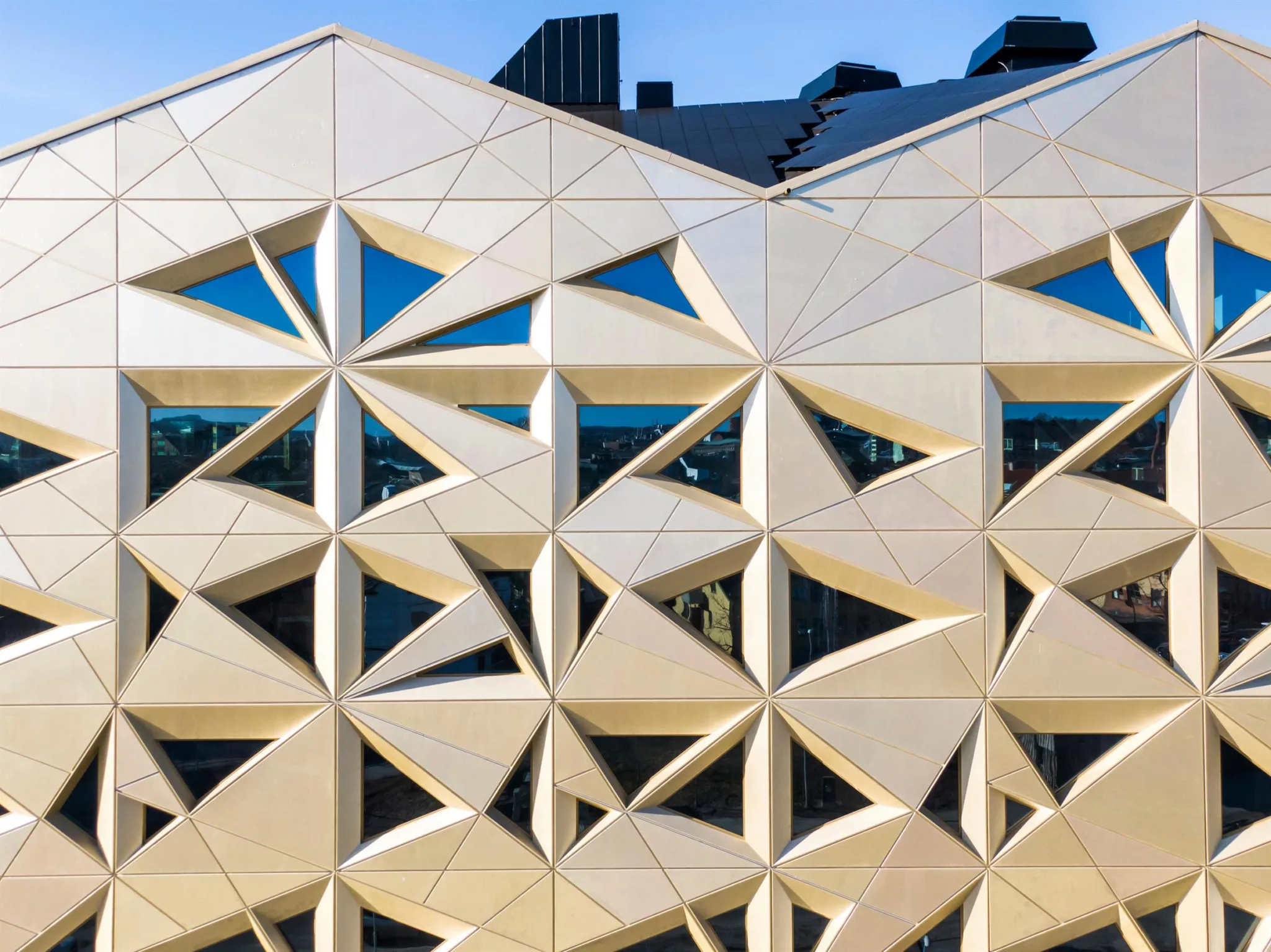 Detaljerad fasad med geometriska, triangulära mönster och glaspartier som reflekterar himlen.