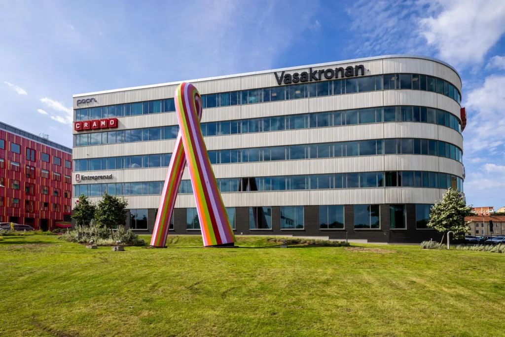 En modern byggnad med fasadskylt för Vasakronan, gräsmatta framför och en stor regnbågsfärgad installation.