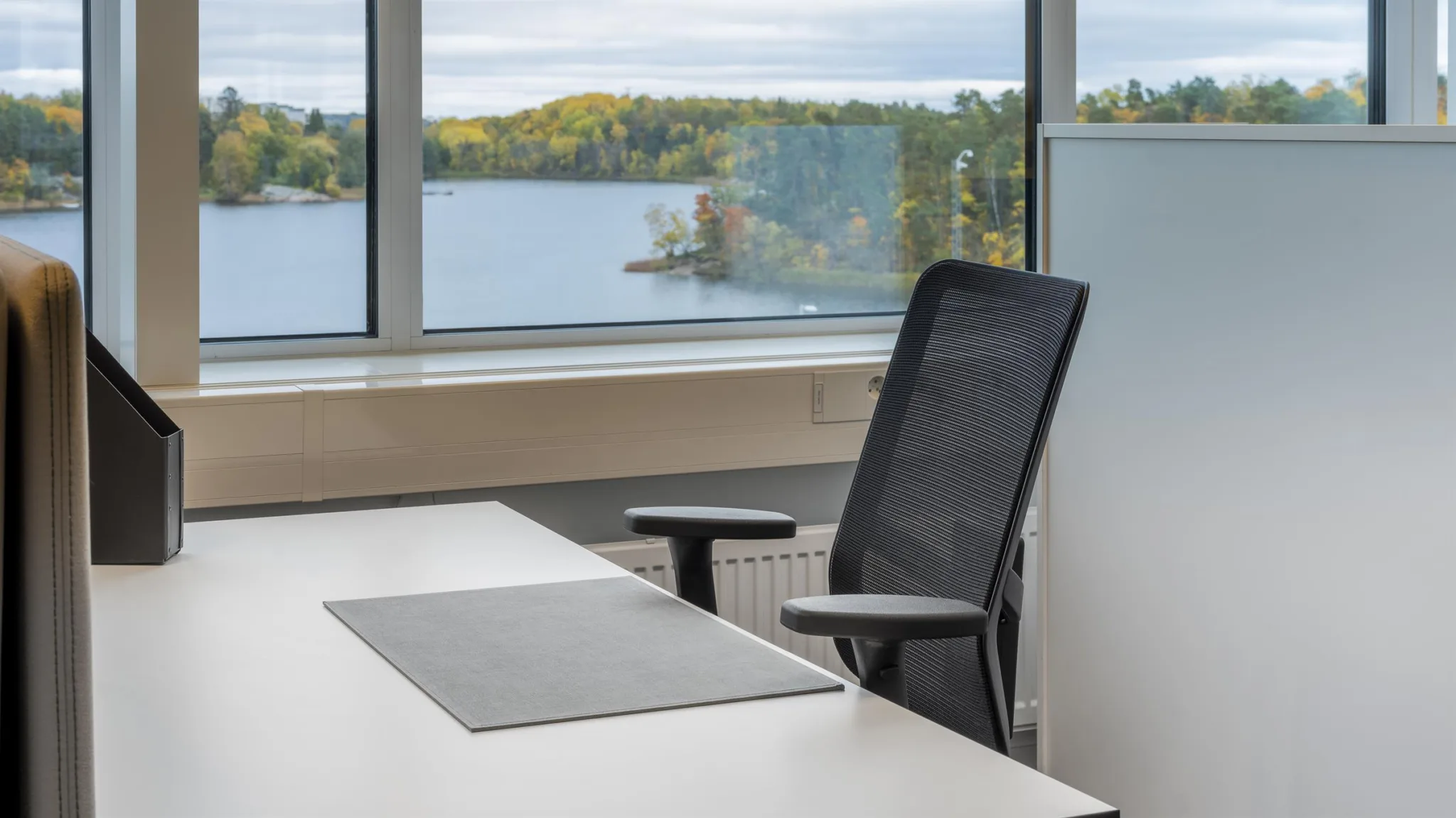 Ett skrivbord med en kontorsstol och utsikt över en sjö genom stora fönster.