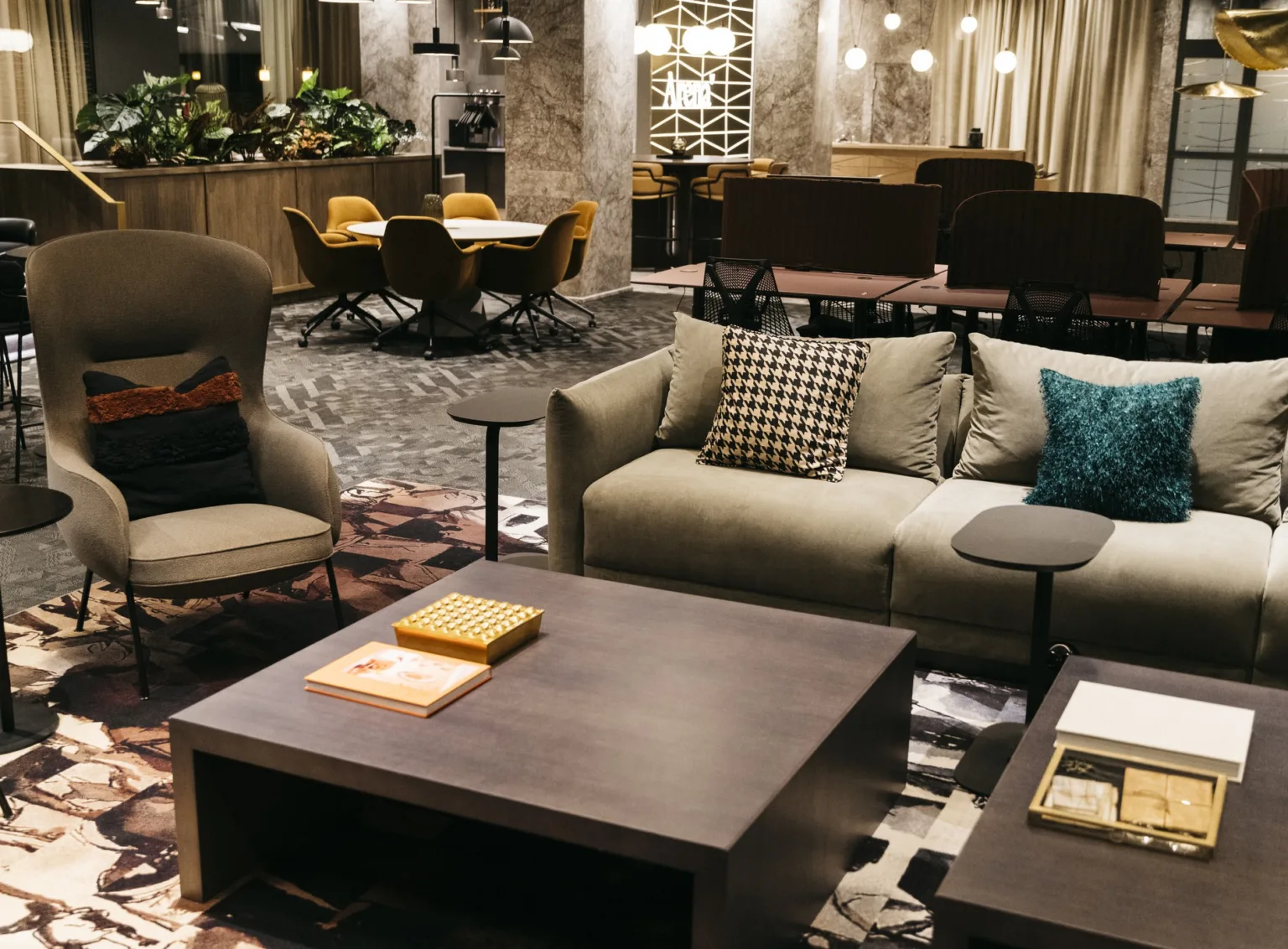 En modern lounge med en soffa, fåtöljer, soffbord och matbord i bakgrunden, omgiven av varma belysningsdetaljer.