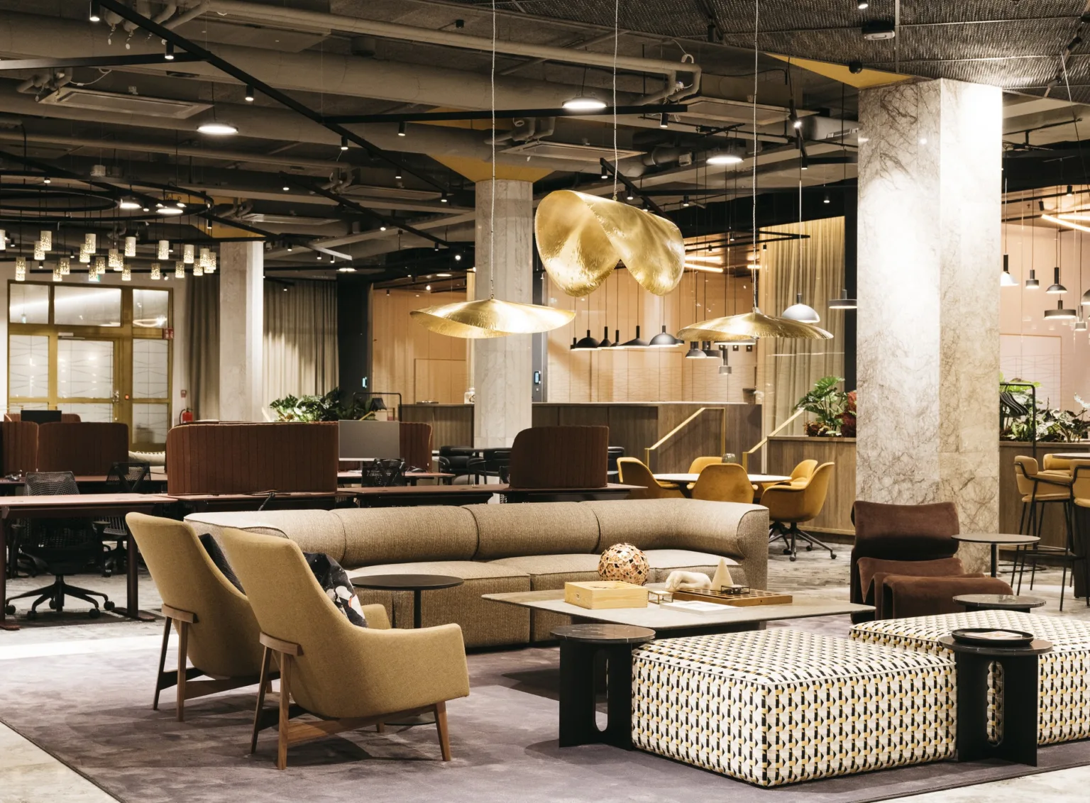 En rymlig lounge med soffor, fåtöljer och hängande lampor i ett industriellt designat utrymme.