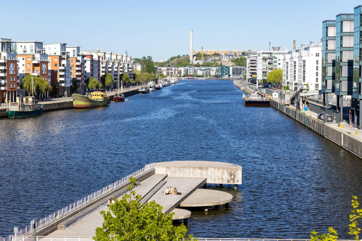 En bred kanal med båtar på båda sidor och moderna byggnader runtom.