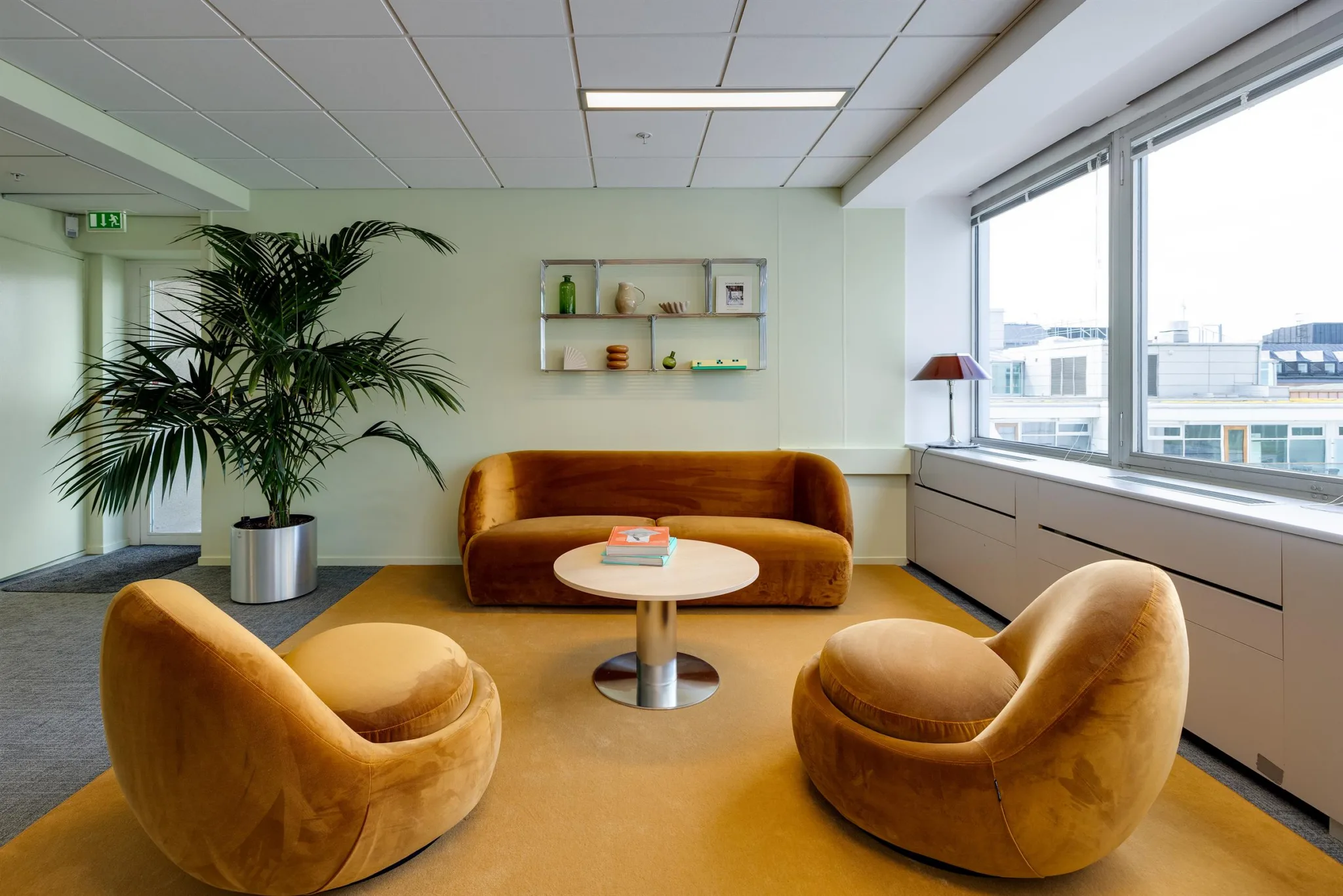 En mysig lounge med en orange soffa, två fåtöljer, ett runt bord, en grön växt och hyllor på väggen.