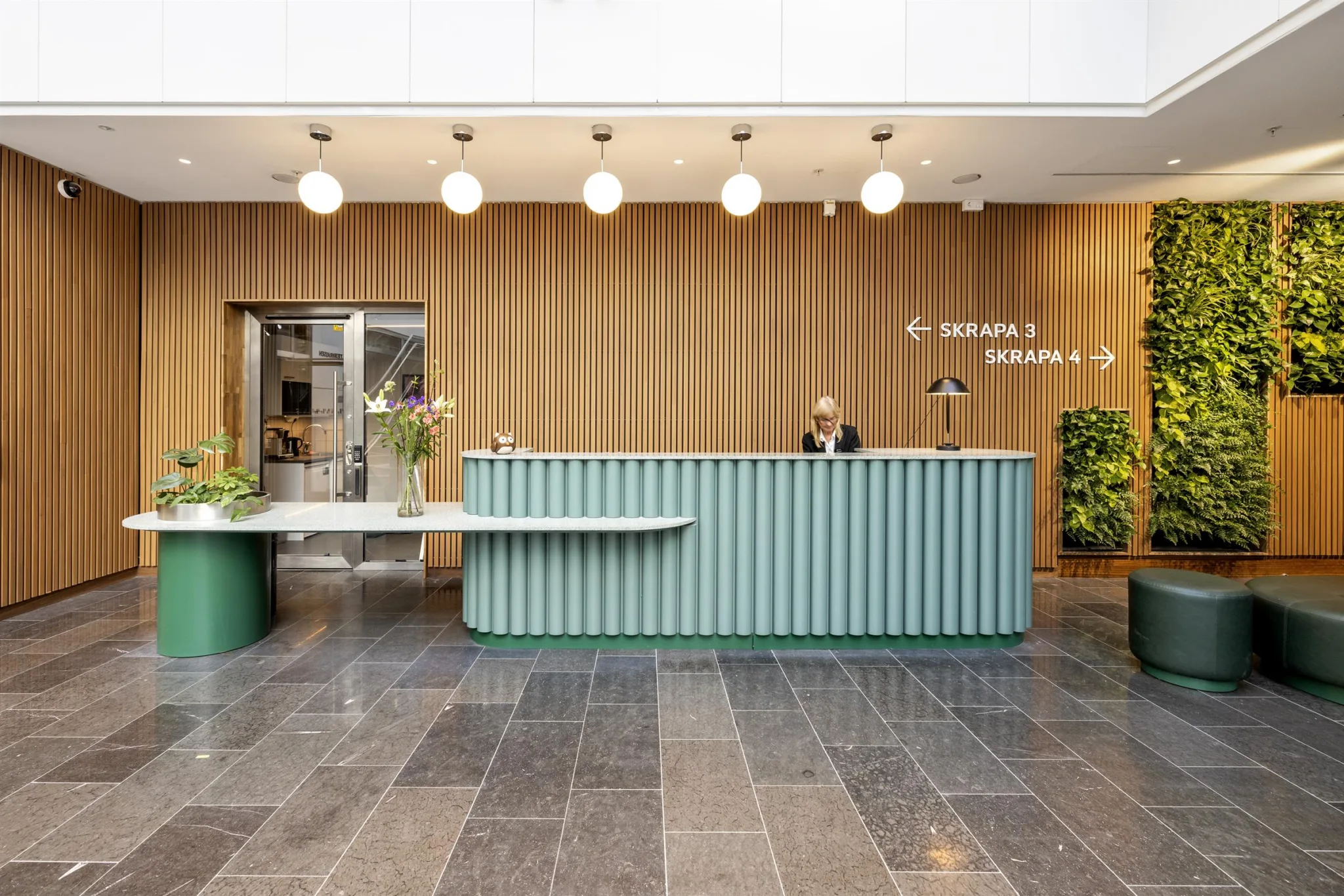 3. En receptionsdisk med grön front, träpaneler i bakgrunden och dekorativa lampor ovanför.