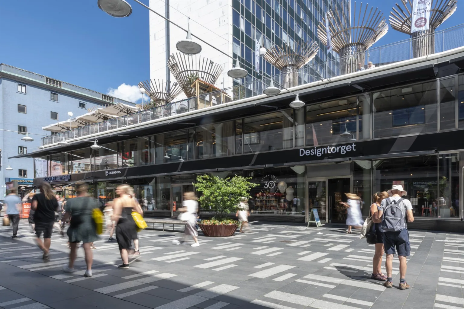 5. Ett torg med människor som går förbi en modern byggnad med glasfasad och butiker.