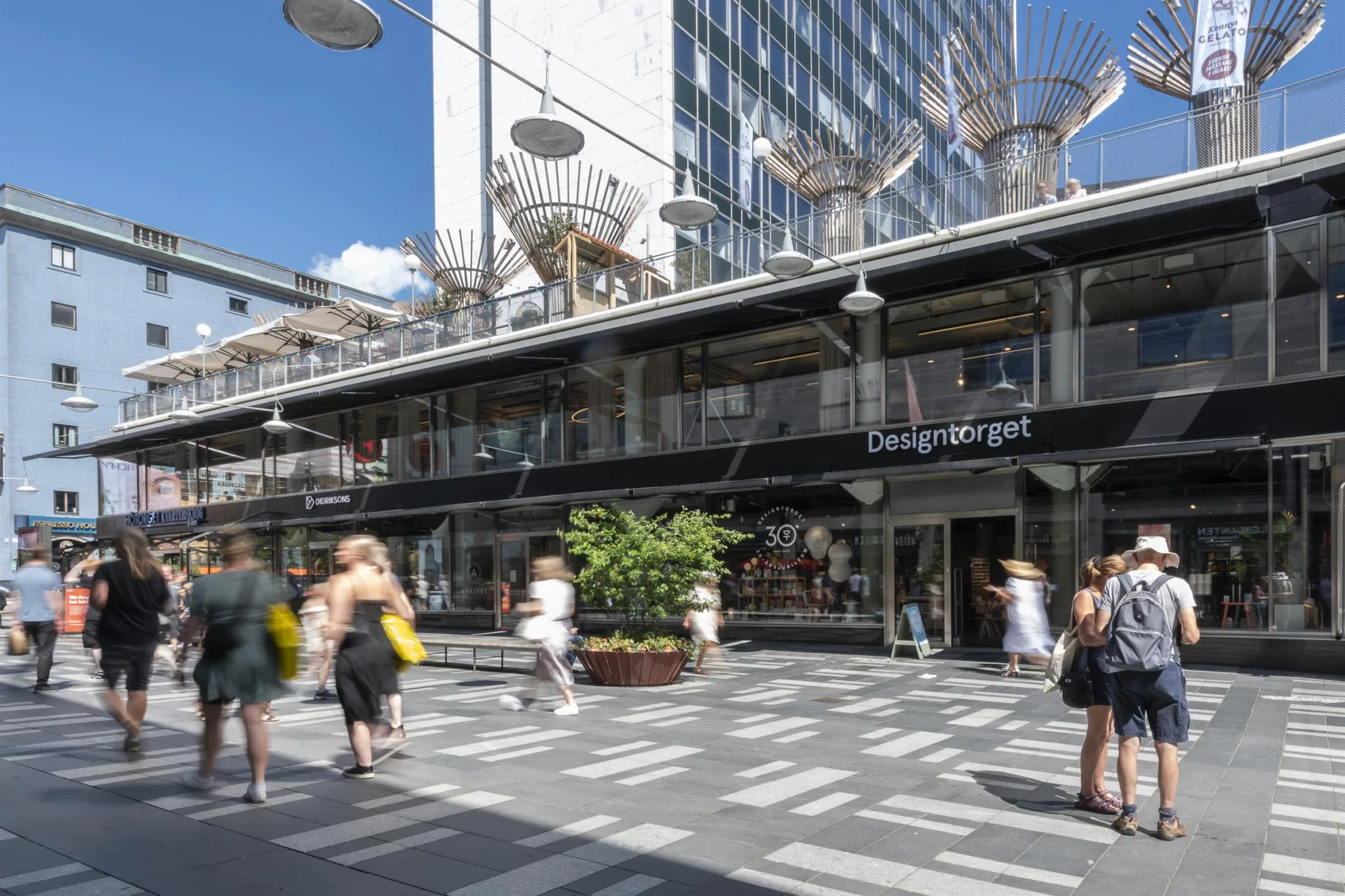 5. Ett torg med människor som går förbi en modern byggnad med glasfasad och butiker.