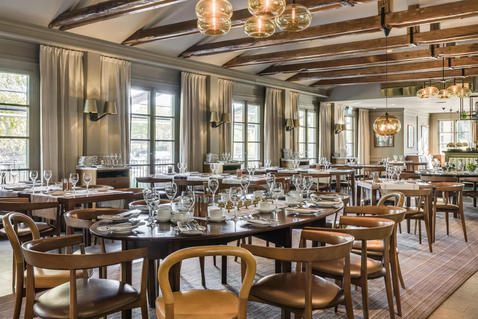 En elegant restaurang med trästolar, dukade bord och fönster som släpper in dagsljus.