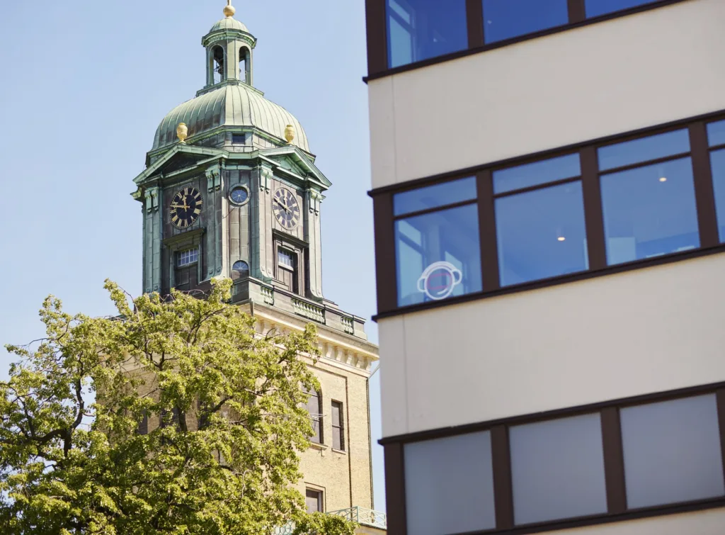 2. En kyrka med ett grönt tak och klocktorn syns bredvid en modern byggnad med glasfönster, med ett träd i förgrunden.