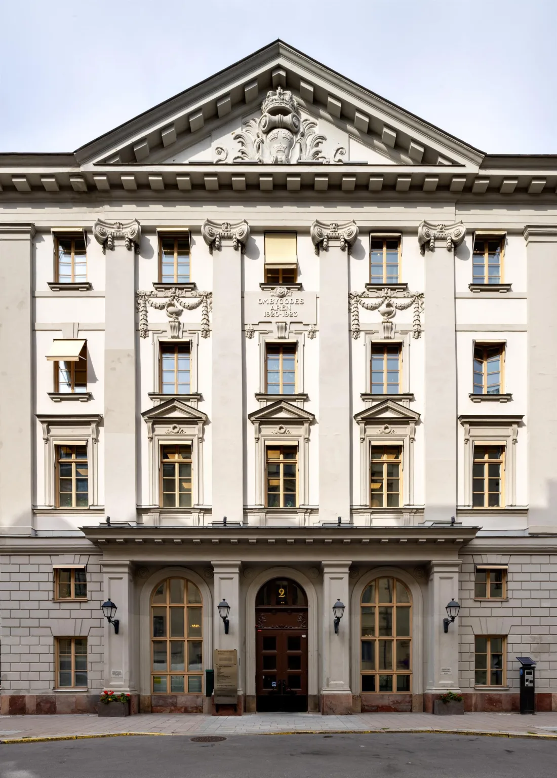 En vit byggnad med klassisk arkitektur, flera fönster och en välvd entré med dekorativa detaljer.