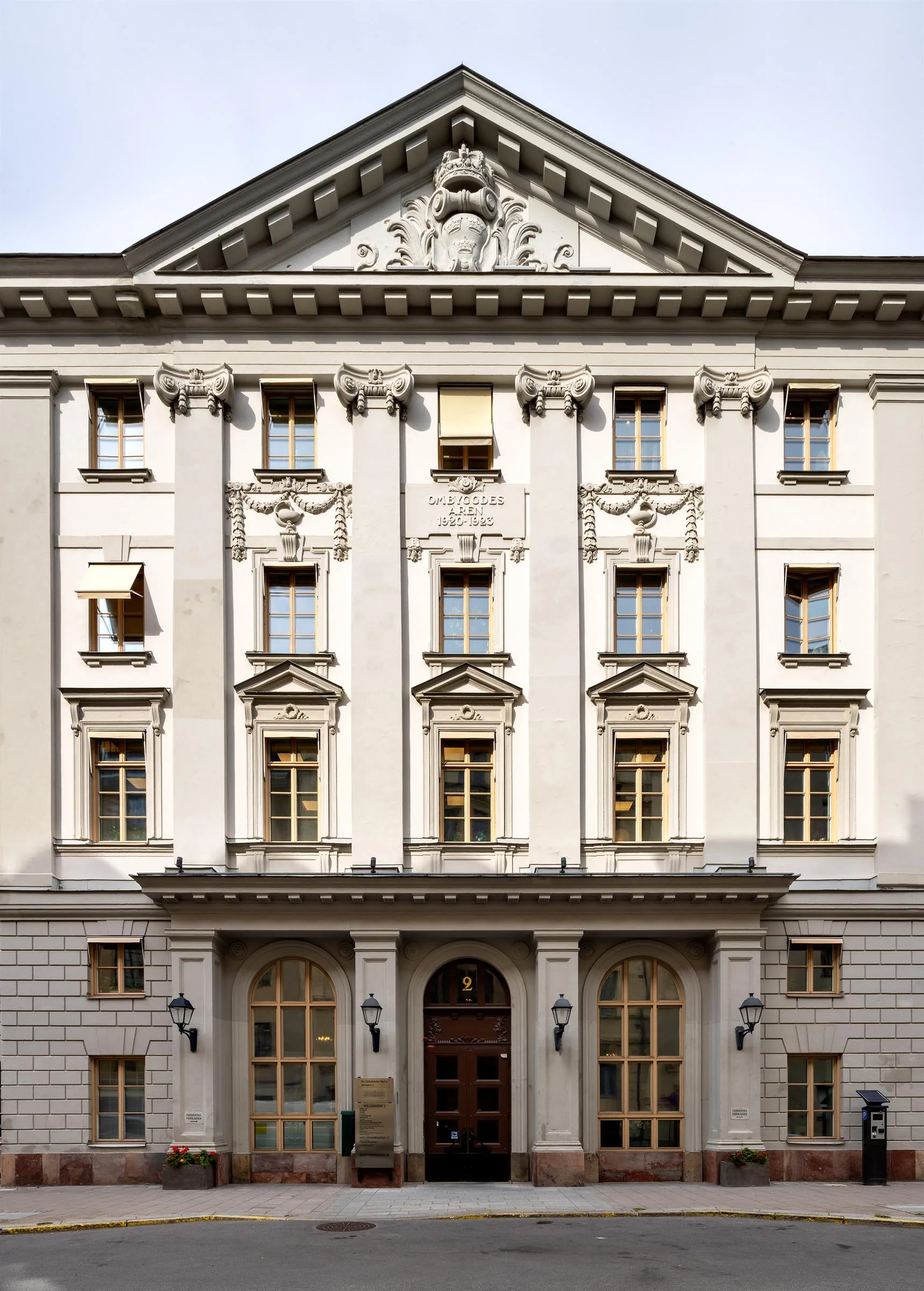 En vit byggnad med klassisk arkitektur, flera fönster och en välvd entré med dekorativa detaljer.