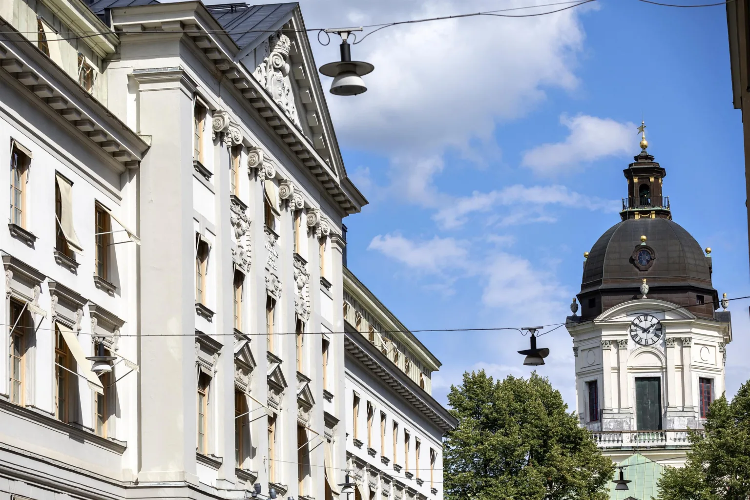 Exteriör av klassiska byggnader med vit fasad, detaljerade dekorationer, gatlampor och en kyrka med kupol i bakgrunden.