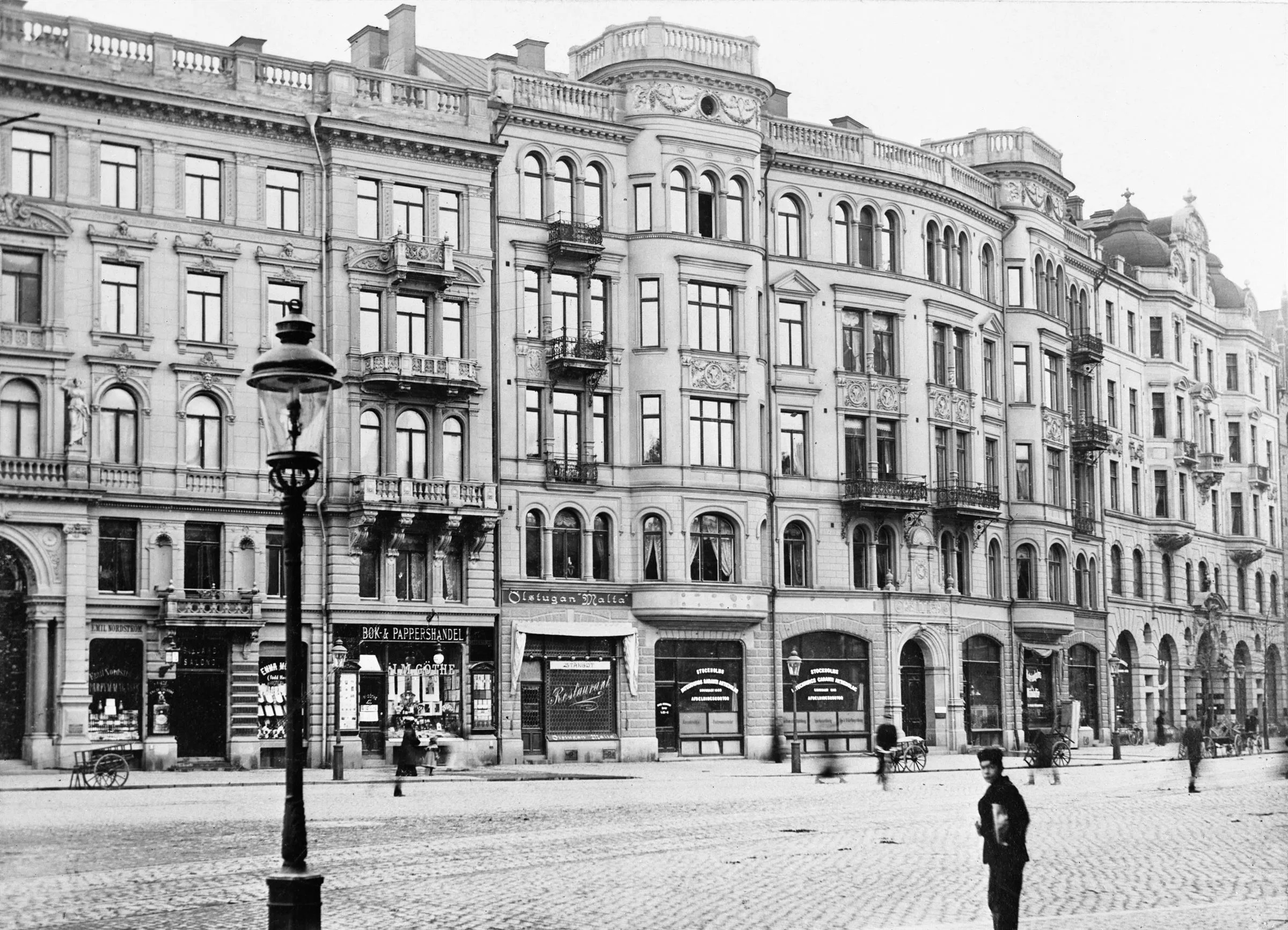 En svartvit bild av en äldre byggnad med flera våningar och butiker på bottenvåningen.
