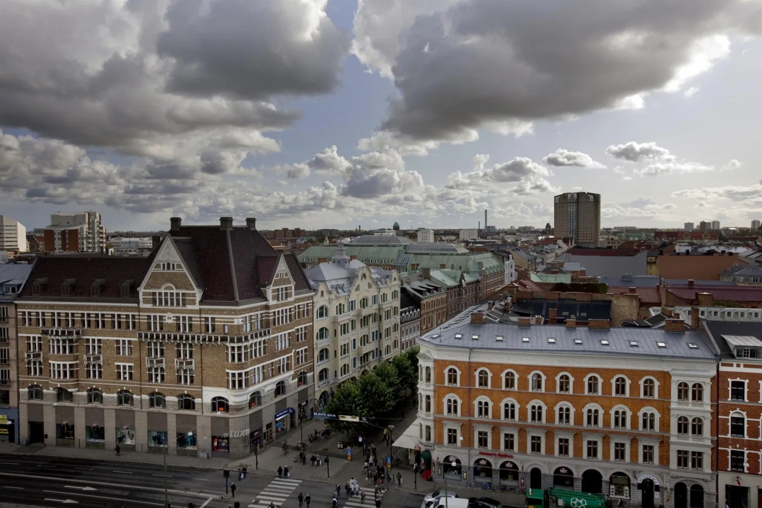 5. En stadsutsikt med gamla byggnader, torg, grönska och molnig himmel.