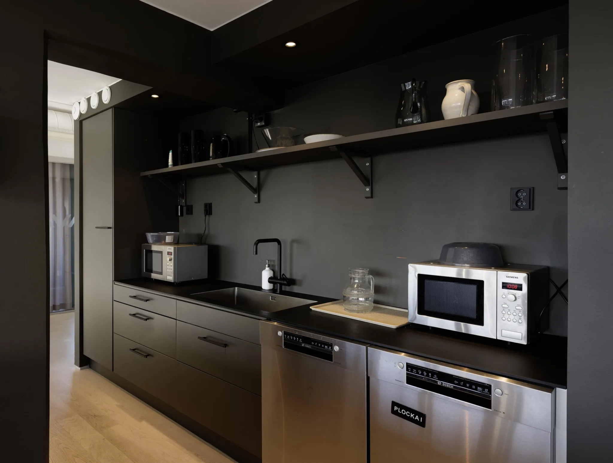 Ett modernt kök med svart inredning, rostfria vitvaror och en mikrovågsugn på bänken.