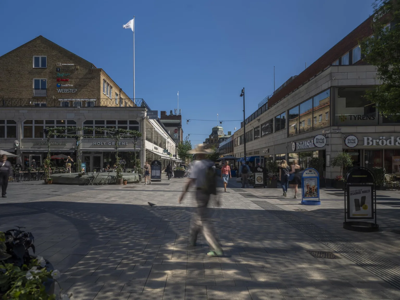 1. En man går över ett torg omgiven av byggnader under en klar blå himmel.