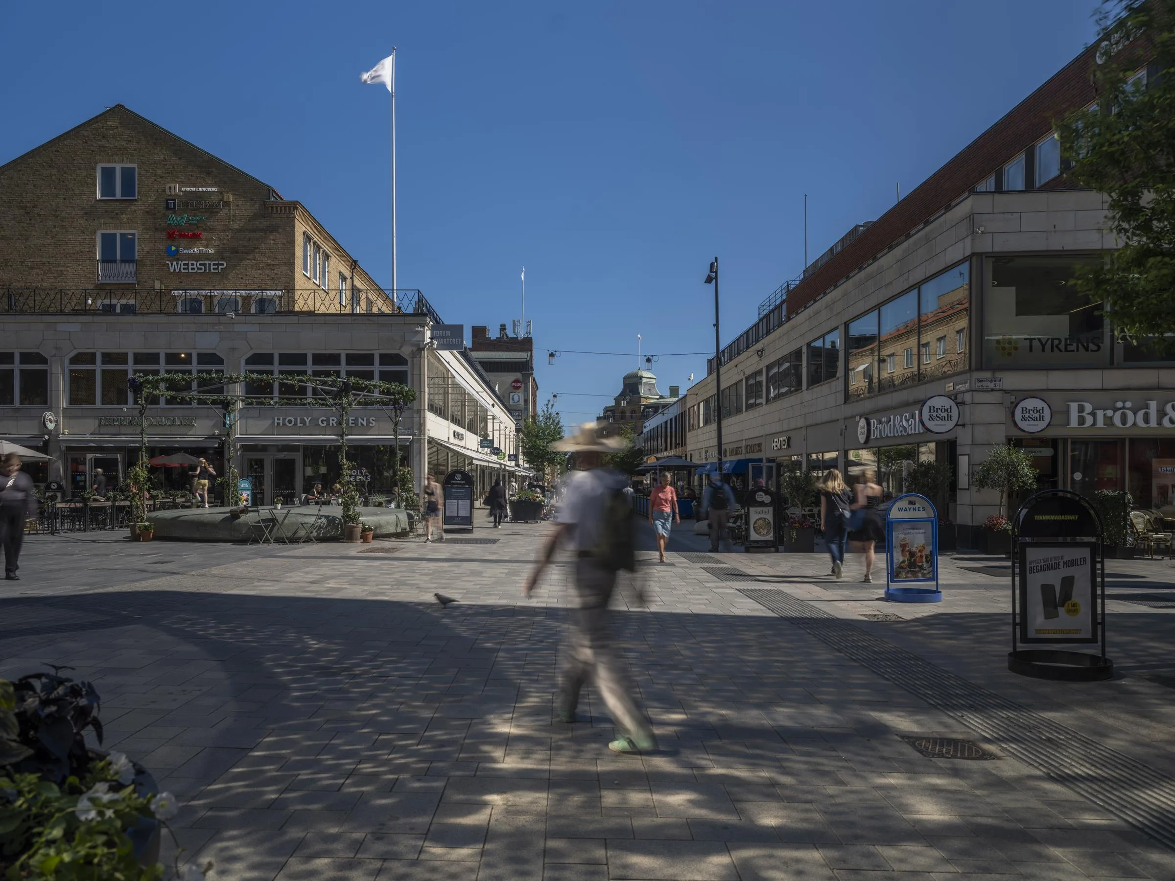 1. En man går över ett torg omgiven av byggnader under en klar blå himmel.