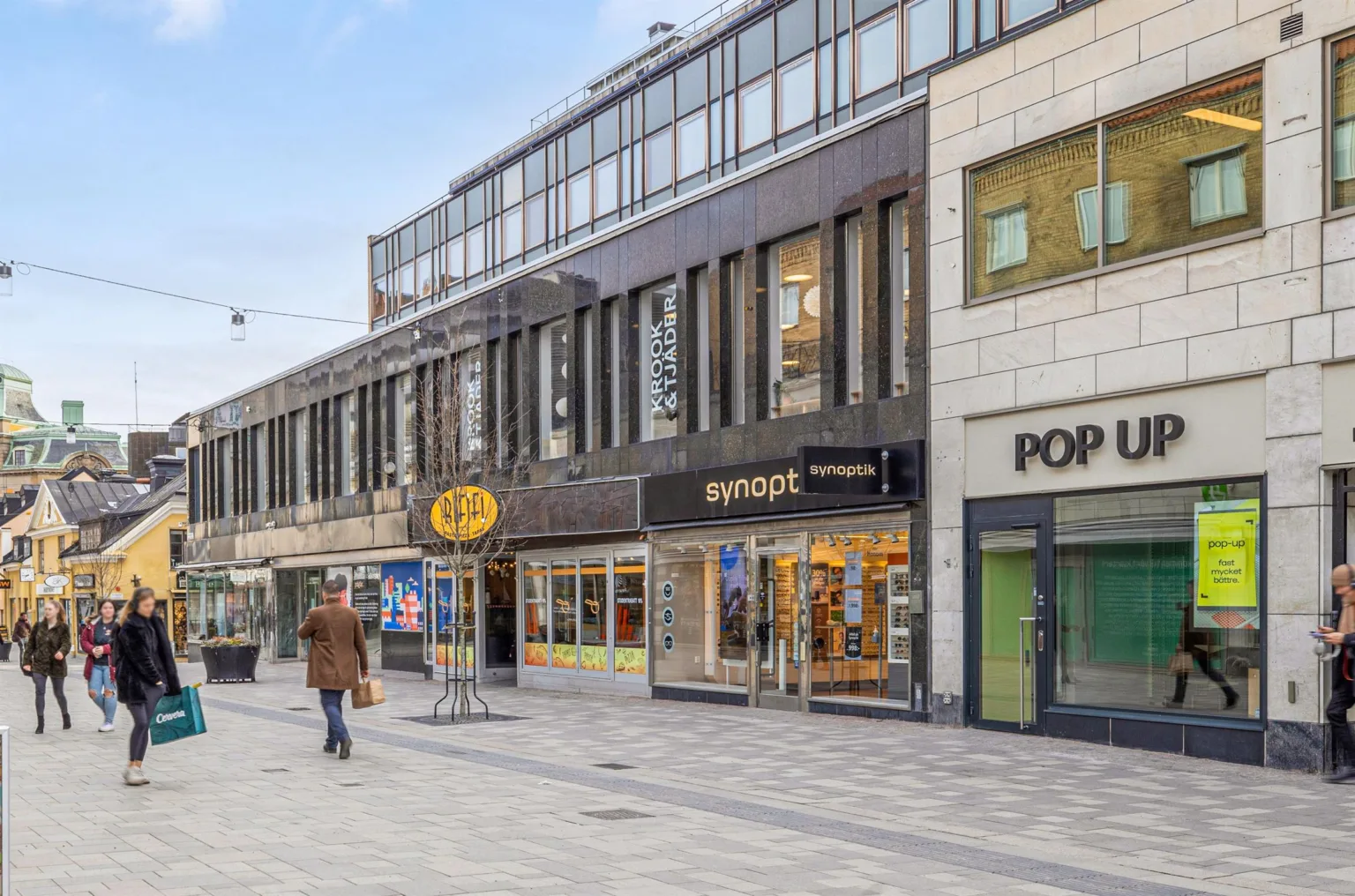 3. En gågata med butiker, inklusive skyltar för "Swopt" och "Pop". En person går med en kasse.