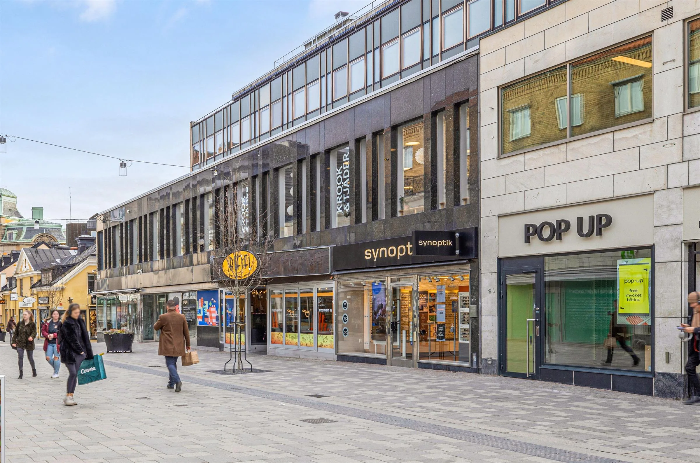 3. En gågata med butiker, inklusive skyltar för "Swopt" och "Pop". En person går med en kasse.