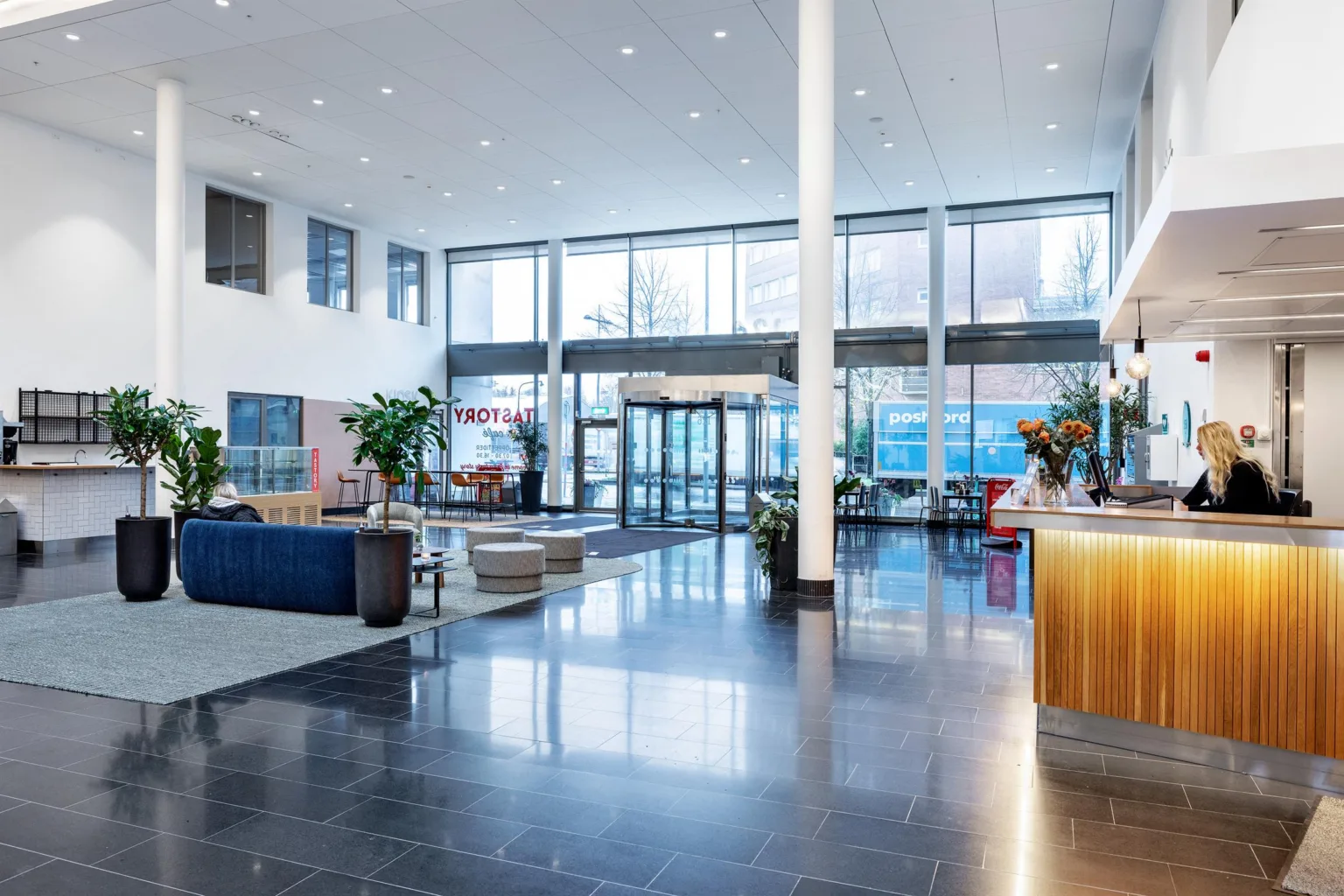 En rymlig lobby med glasentré, sittgrupper, växter och en reception med trädetaljer.