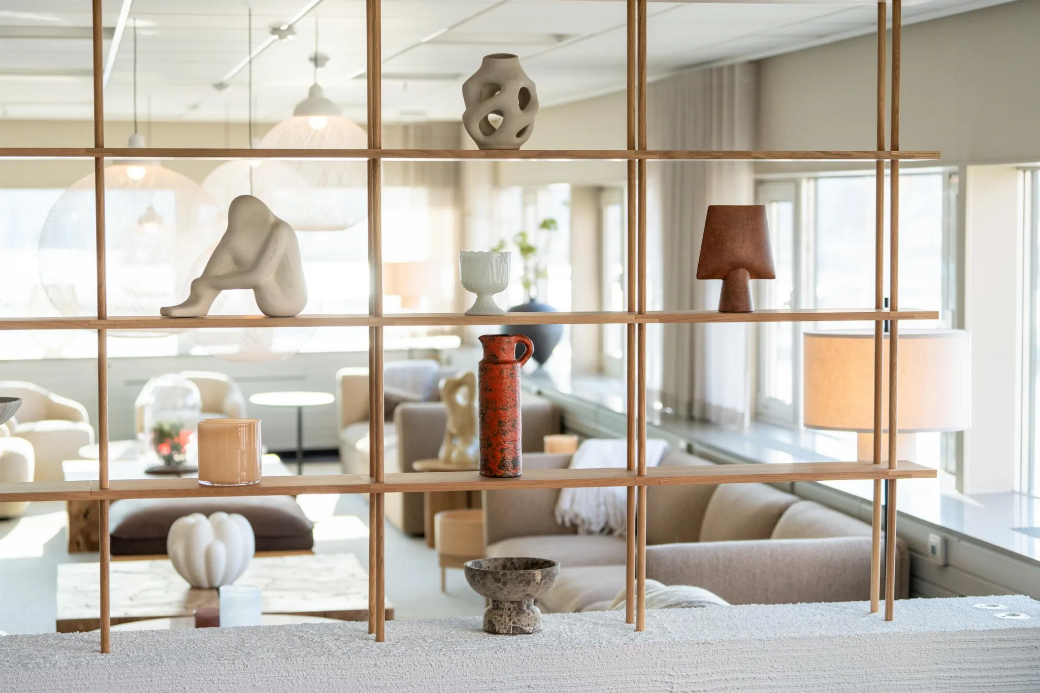 En hylla med dekorativa föremål som skulpturer och lampor, med en lounge i bakgrunden.