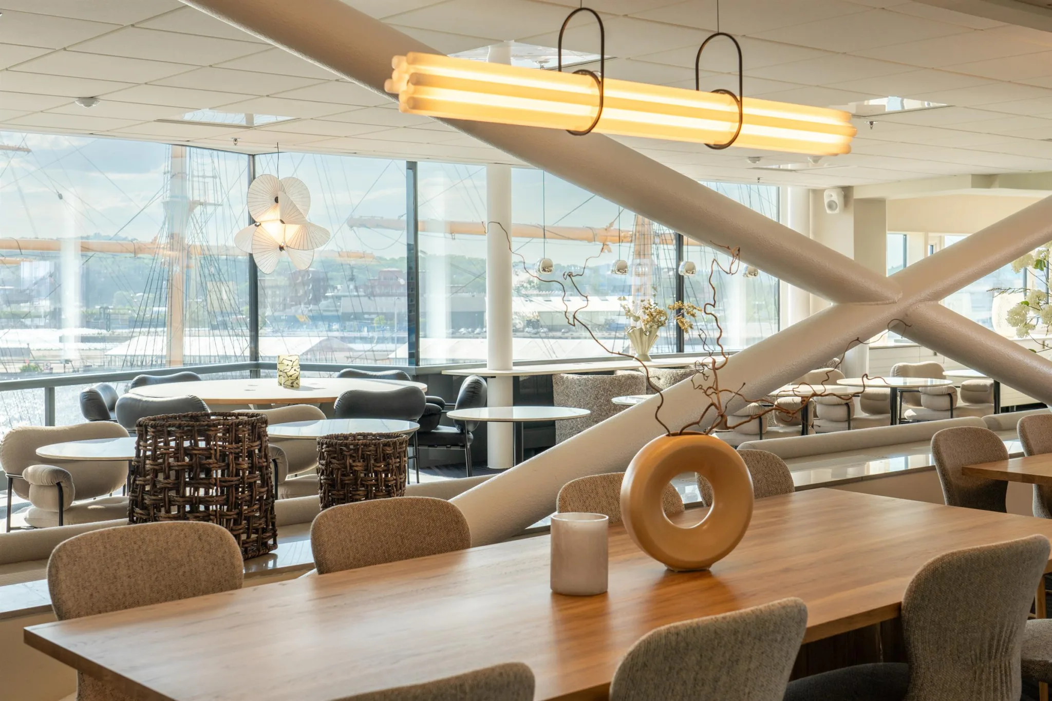Ett träbord med stolar, dekorativa föremål och moderna hängande lampor, med utsikt över en ljus lokal.