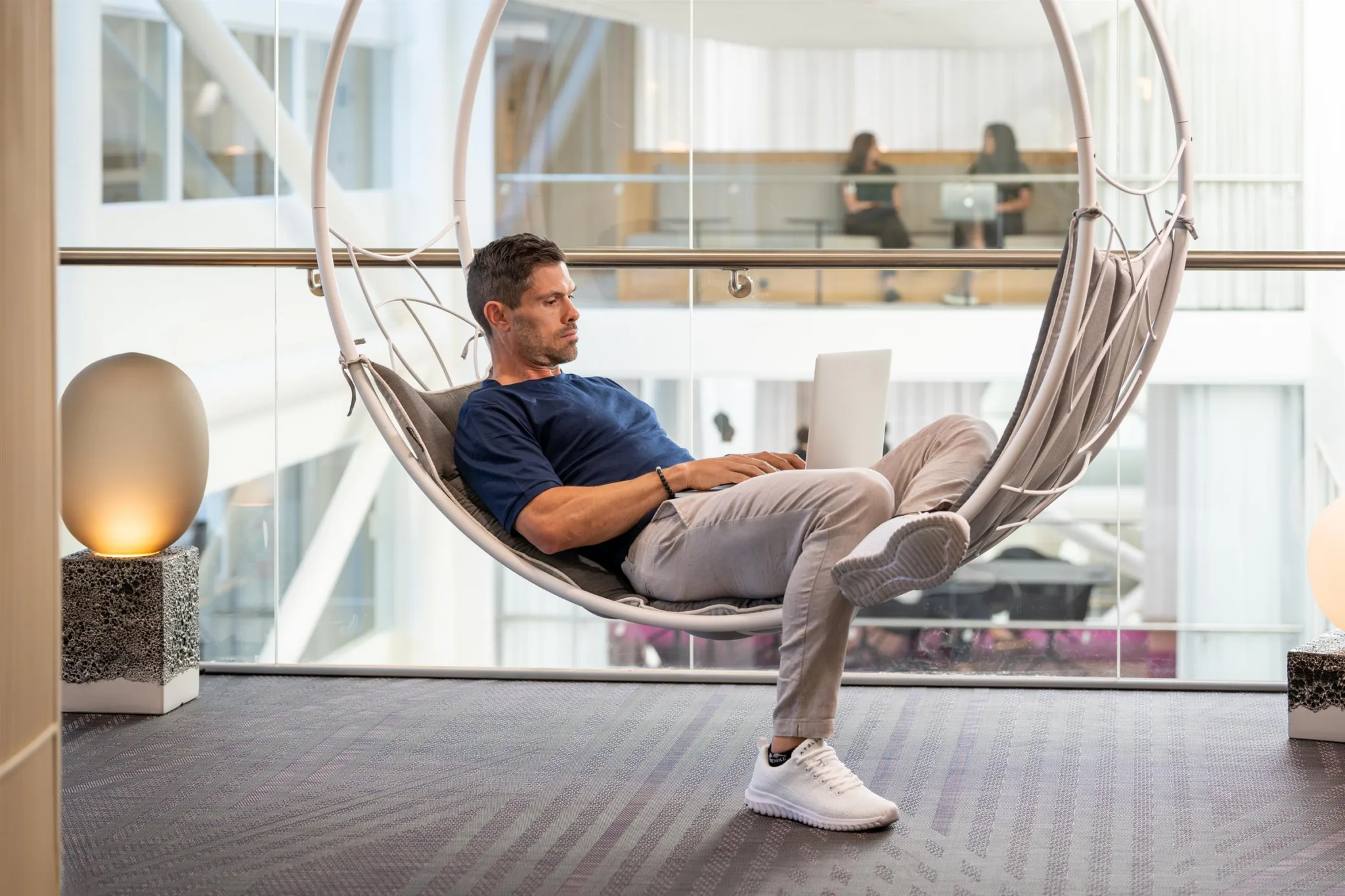 En man sitter i en hängande stol med en laptop och tittar framåt i en modern kontorsmiljö.