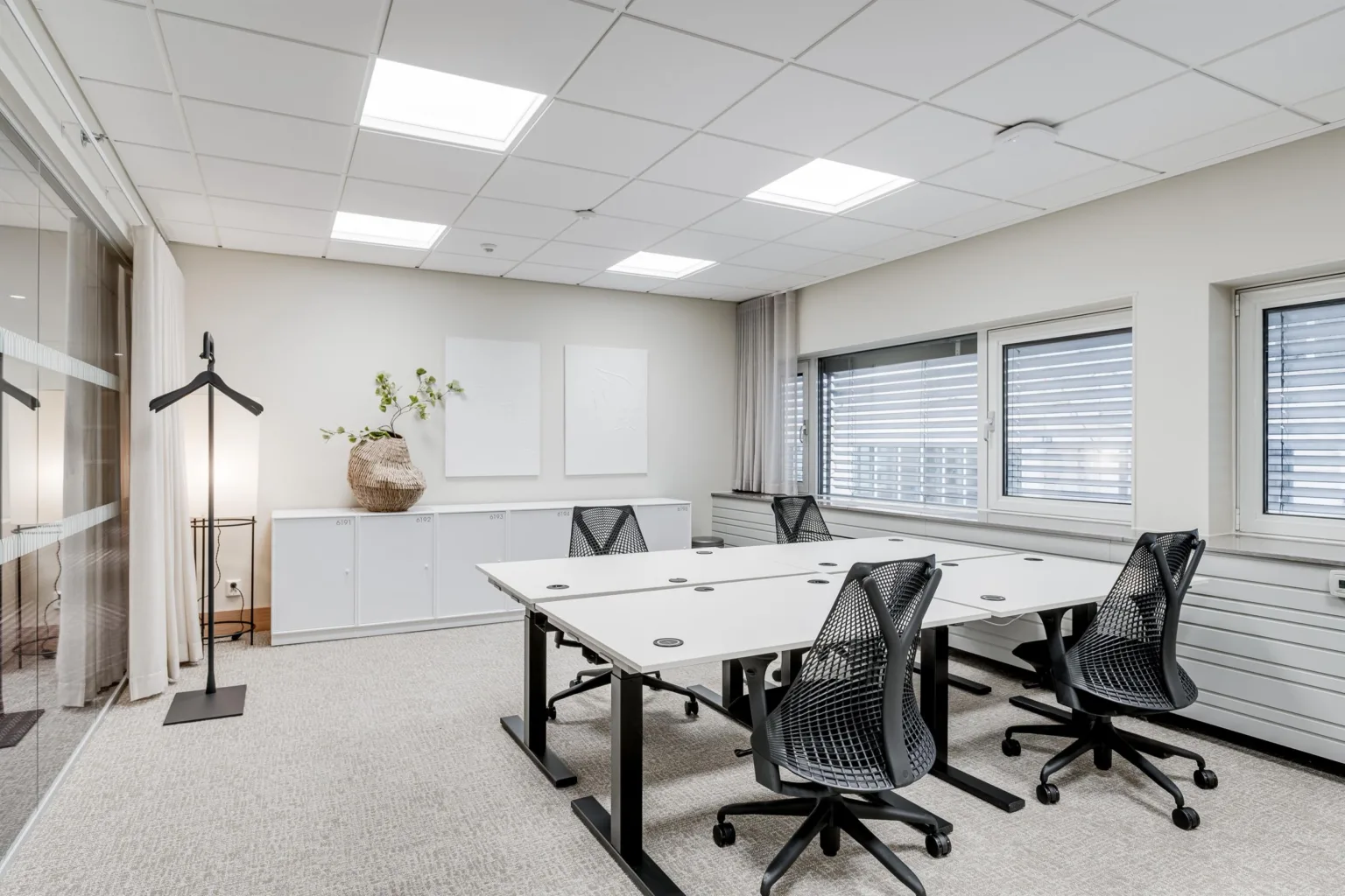 Ett ljust och minimalistiskt kontorsrum med fyra skrivbord och ergonomiska stolar.