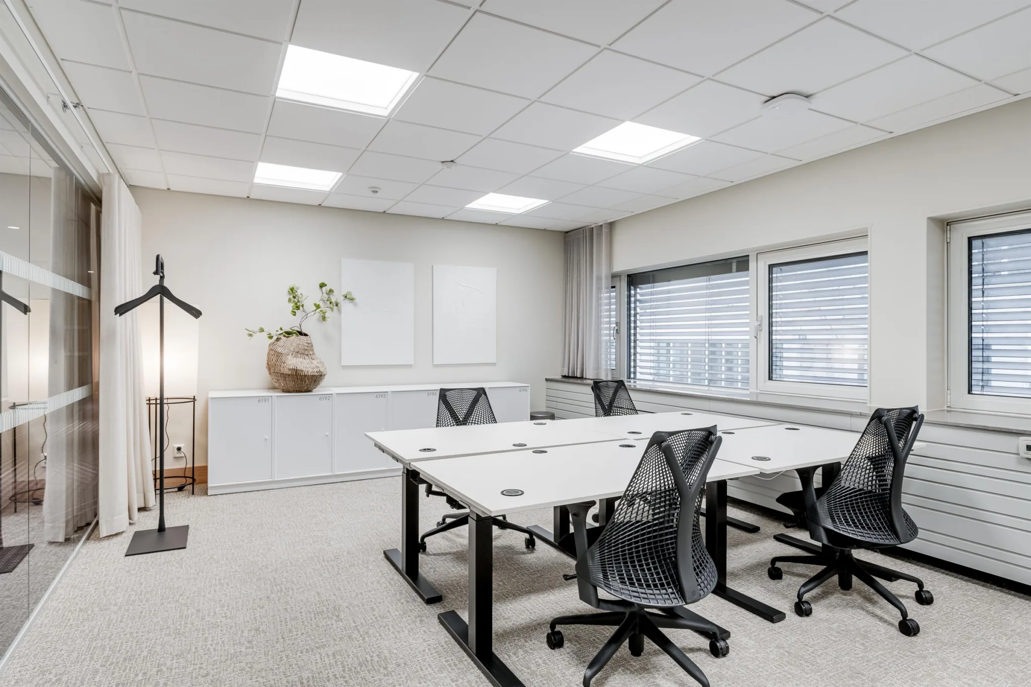 Ett ljust och minimalistiskt kontorsrum med fyra skrivbord och ergonomiska stolar.
