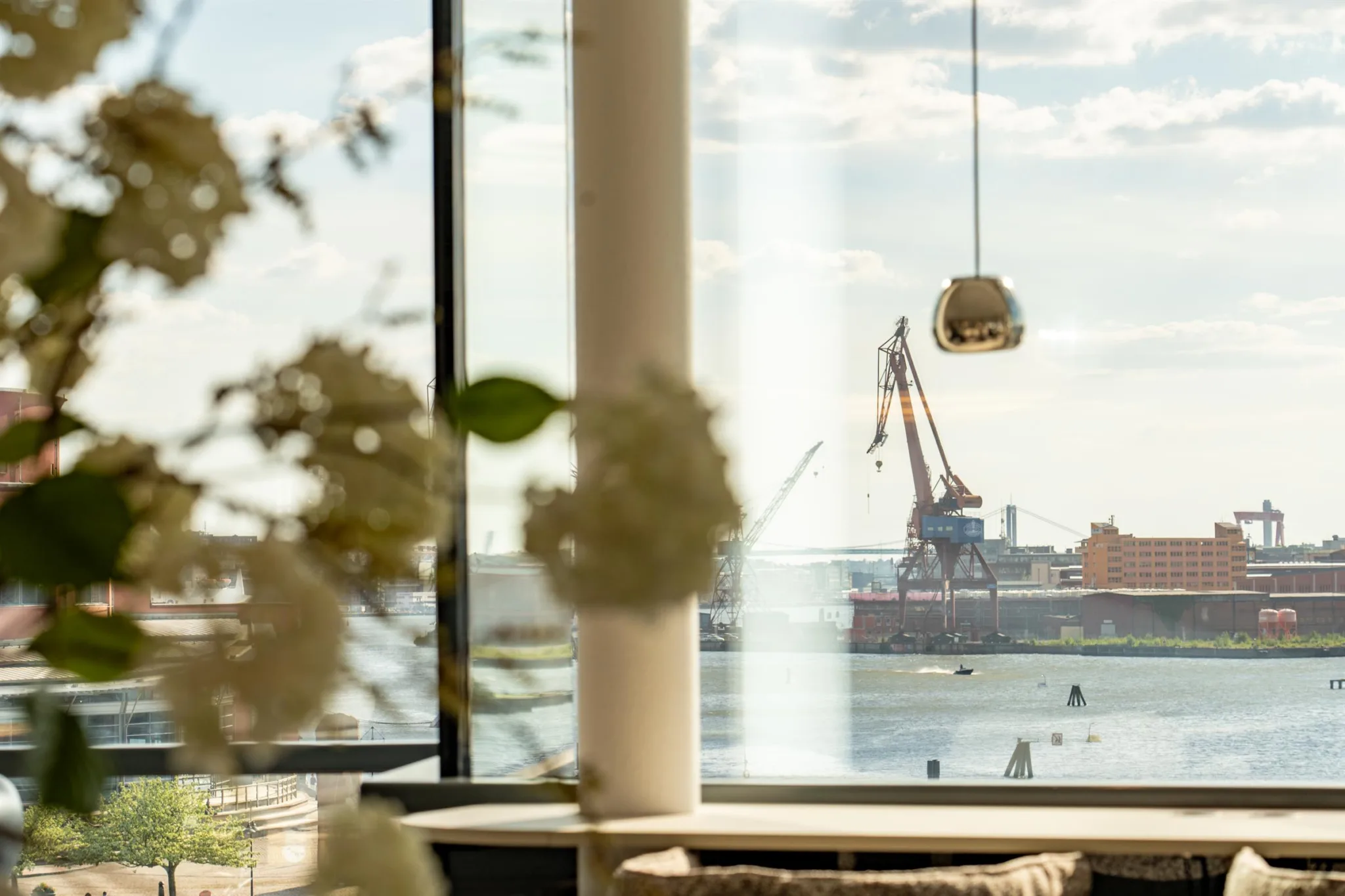 3. Utsikt genom ett fönster med fokus på en kran vid en hamn, dekorerat med vita blommor i förgrunden.