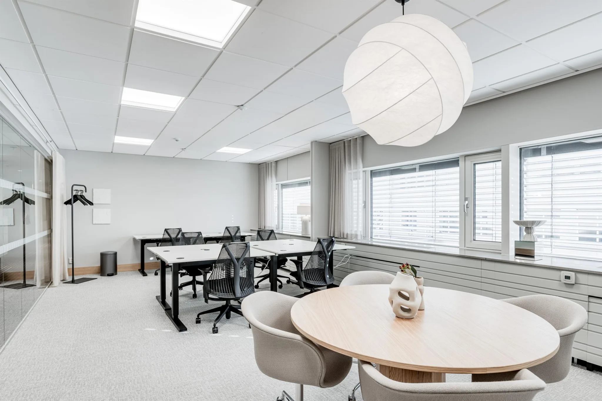 Ett kontorsutrymme med skrivbord, stolar och ett runt bord, dekorerat med en modern hängande lampa.