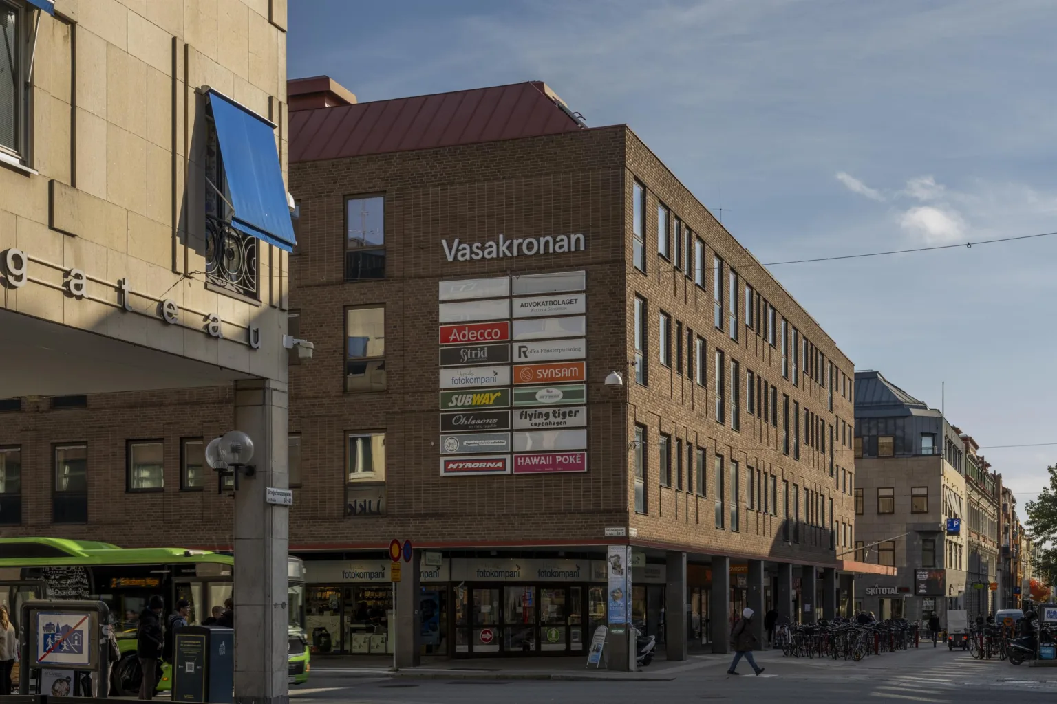 Brun tegelbyggnad med texten "Vasakronan" och fönster täckta med olika färgade skyltar.