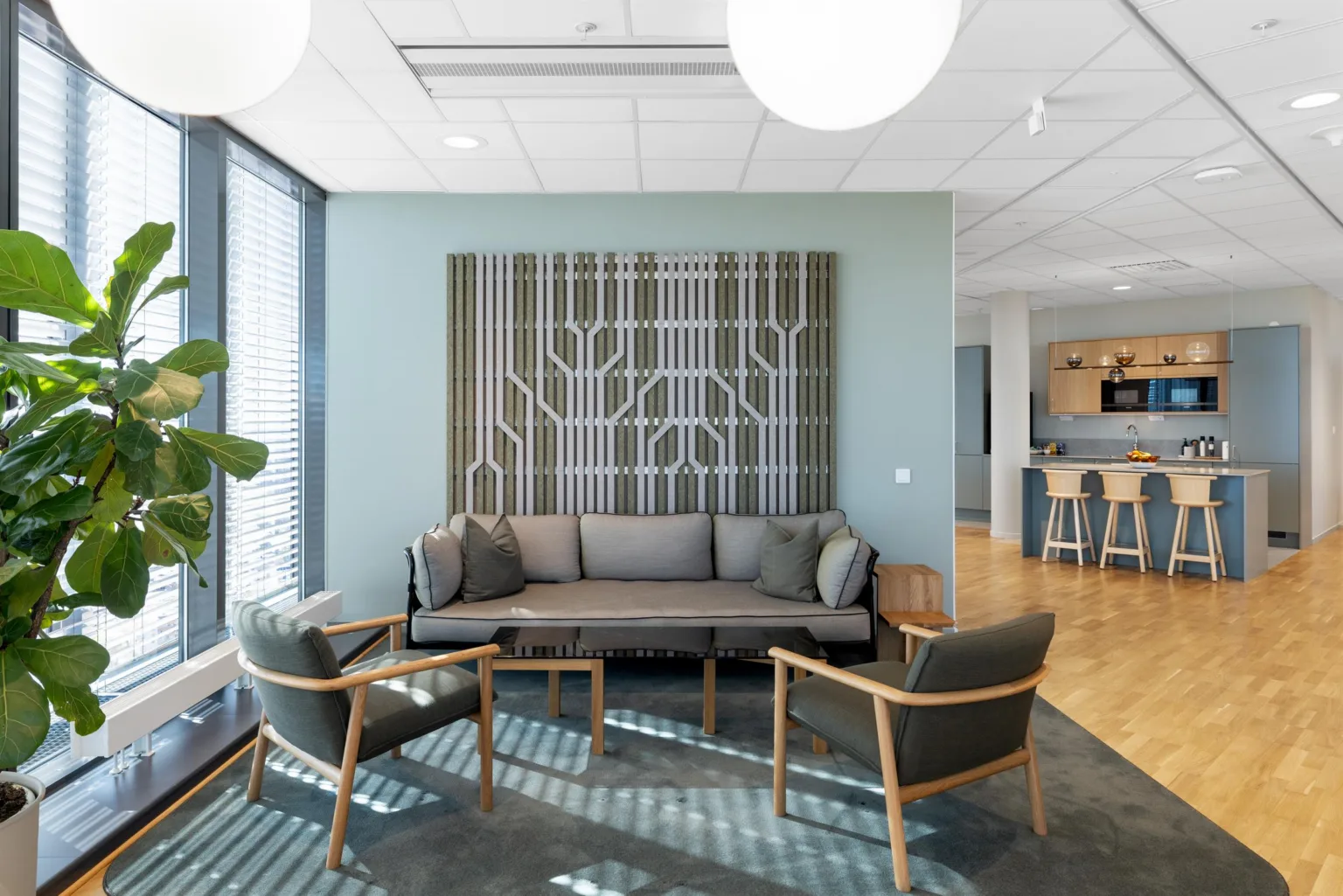En sittgrupp med en grå soffa och två stolar står i ett ljust rum med ett abstrakt konstverk på väggen.