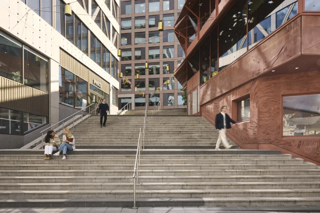 En bred trappa mellan två byggnader, där några personer promenerar upp och ned. En sittande grupp syns vid trappans fot.