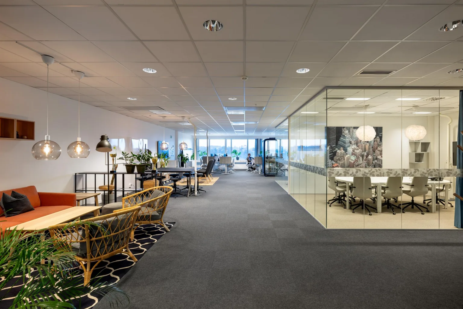 3. Ett kontor med en loungeyta med rottingmöbler och växter, samt ett glasrum till höger.