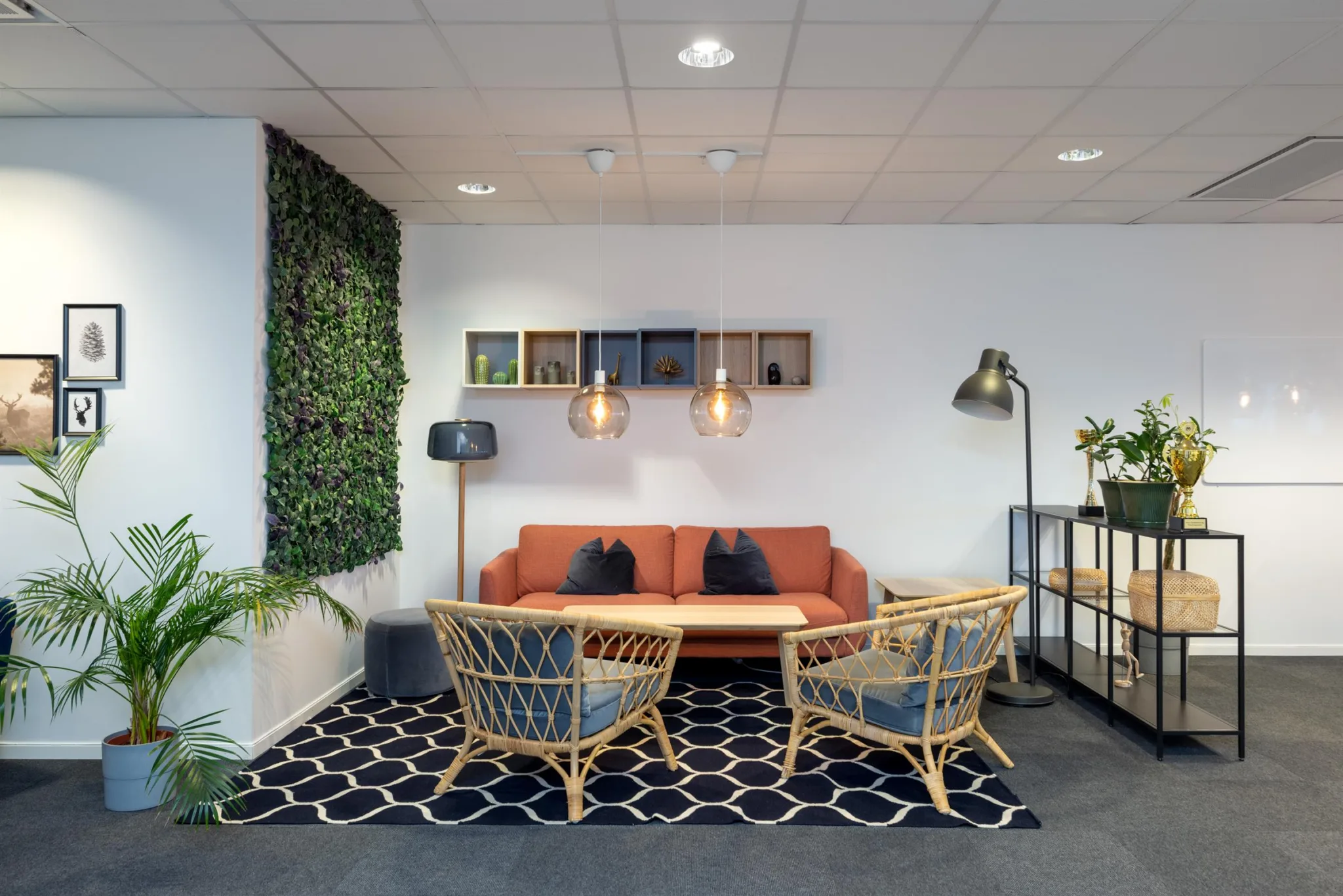 2. En sittgrupp med en orange soffa, två flätade fåtöljer och ett träbord, omgiven av väggdekorationer, lampor och växter.
