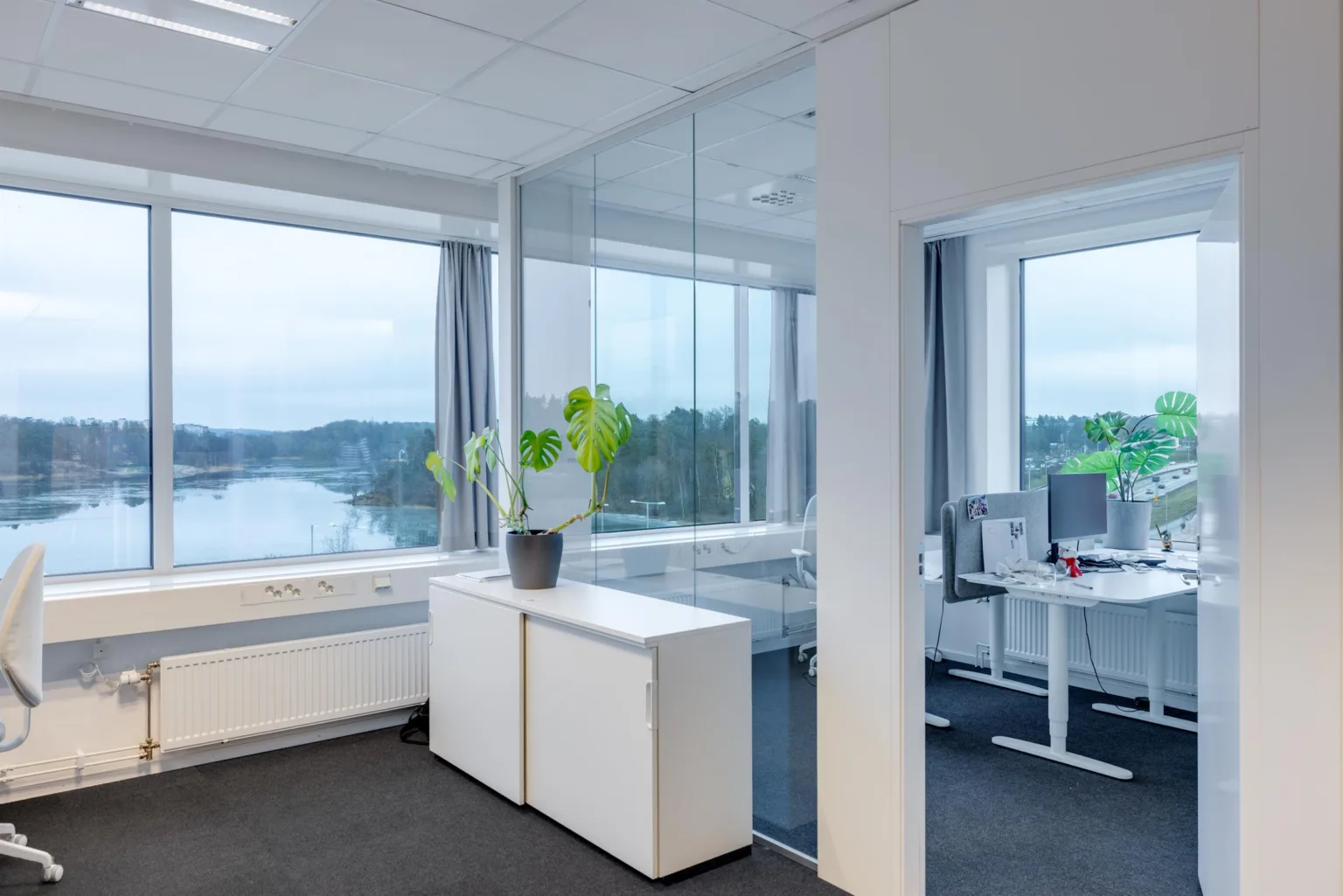 3. Ett kontor med glasväggar, vita möbler och utsikt över en sjö genom stora fönster.