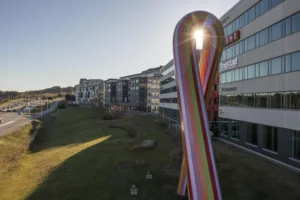 1. En stor färgglad skulptur i form av ett band står på en gräsmatta framför moderna kontorsbyggnader i dagsljus.