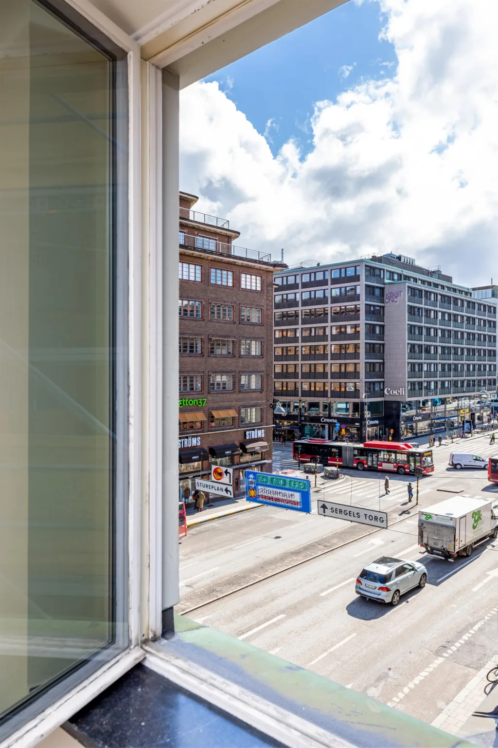 4. Utsikt från ett fönster över en livlig stadsgata med bussar, bilar och flerbostadshus.