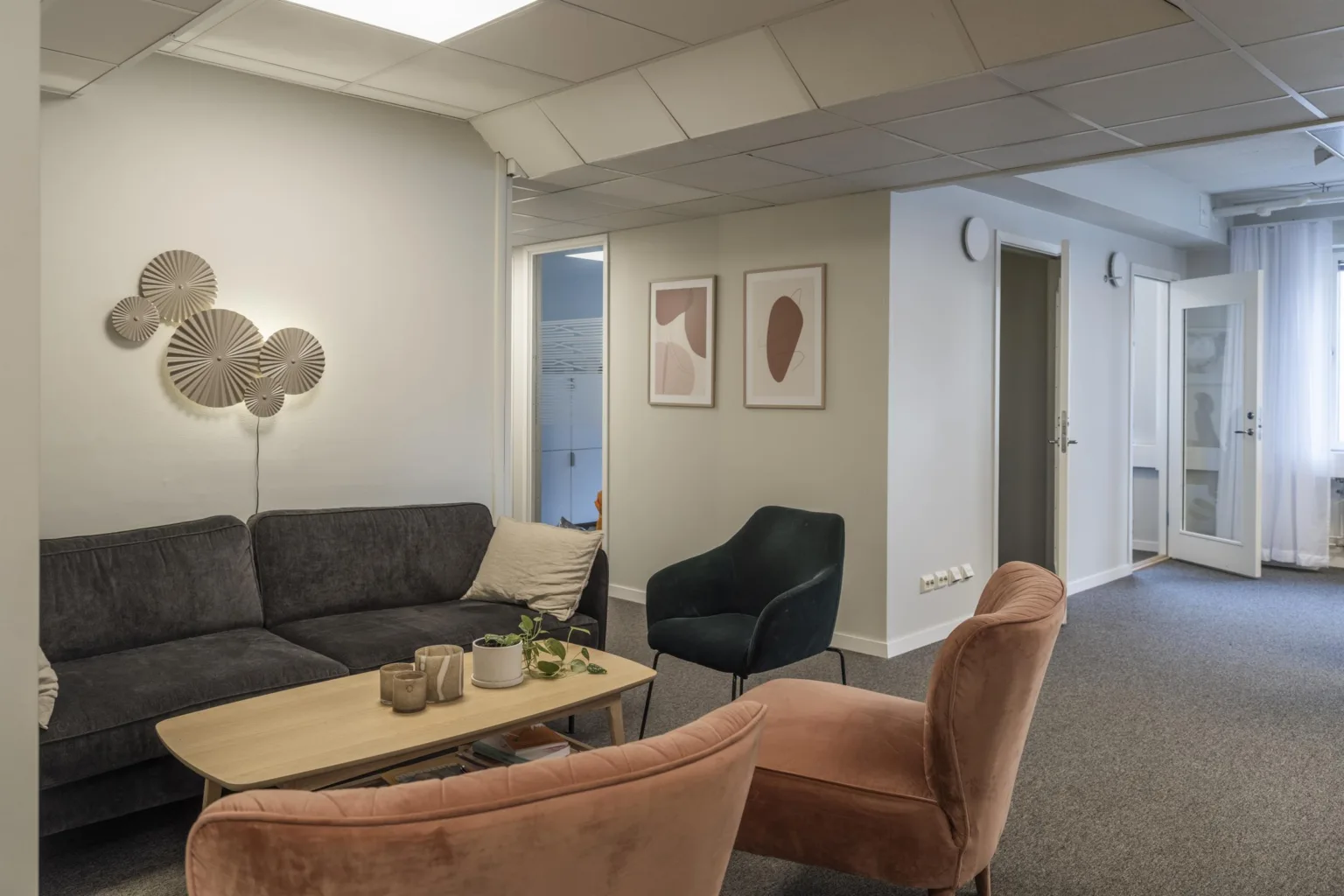 3. Loungeområde med en mörkgrå soffa, en beige fåtölj, en rosa fåtölj och ett soffbord med dekorativa föremål; väggkonst hänger på väggen.