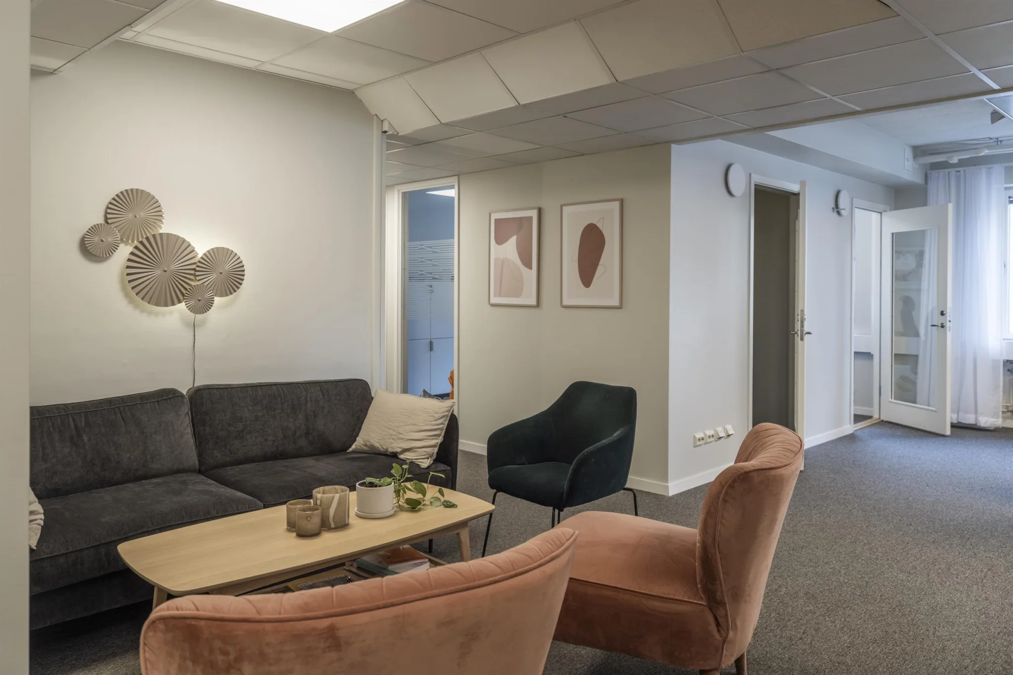 3. Loungeområde med en mörkgrå soffa, en beige fåtölj, en rosa fåtölj och ett soffbord med dekorativa föremål; väggkonst hänger på väggen.