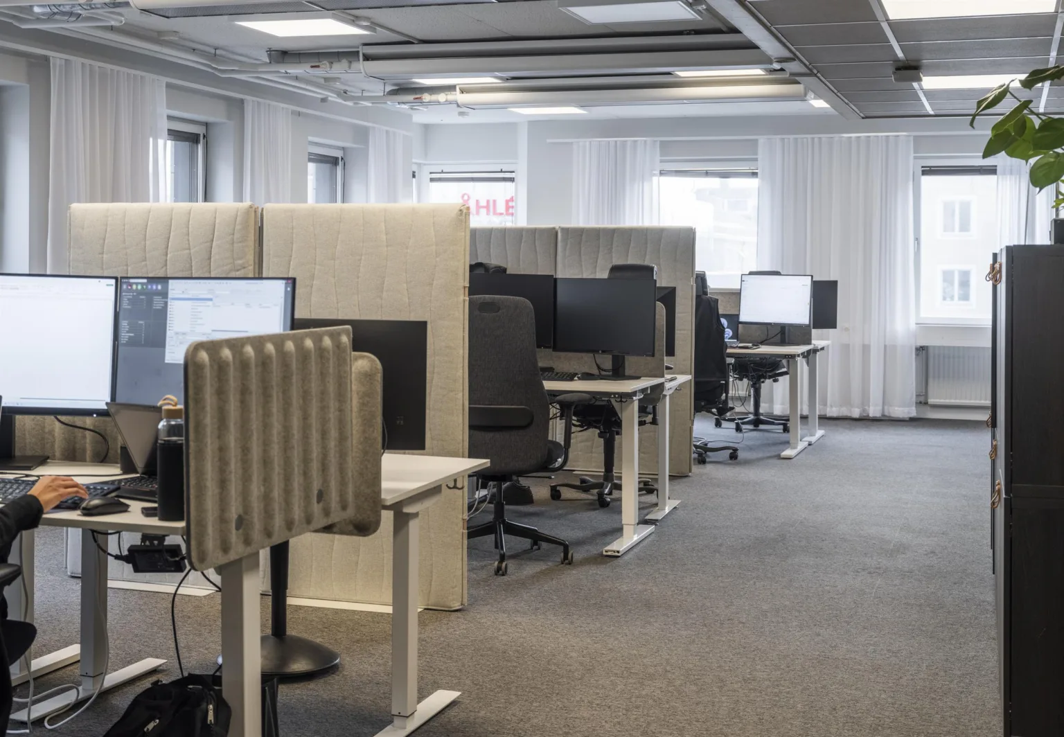 4. Öppet kontorslandskap med skrivbord, datorskärmar och ergonomiska stolar, separerade av ljudabsorberande skärmar.
