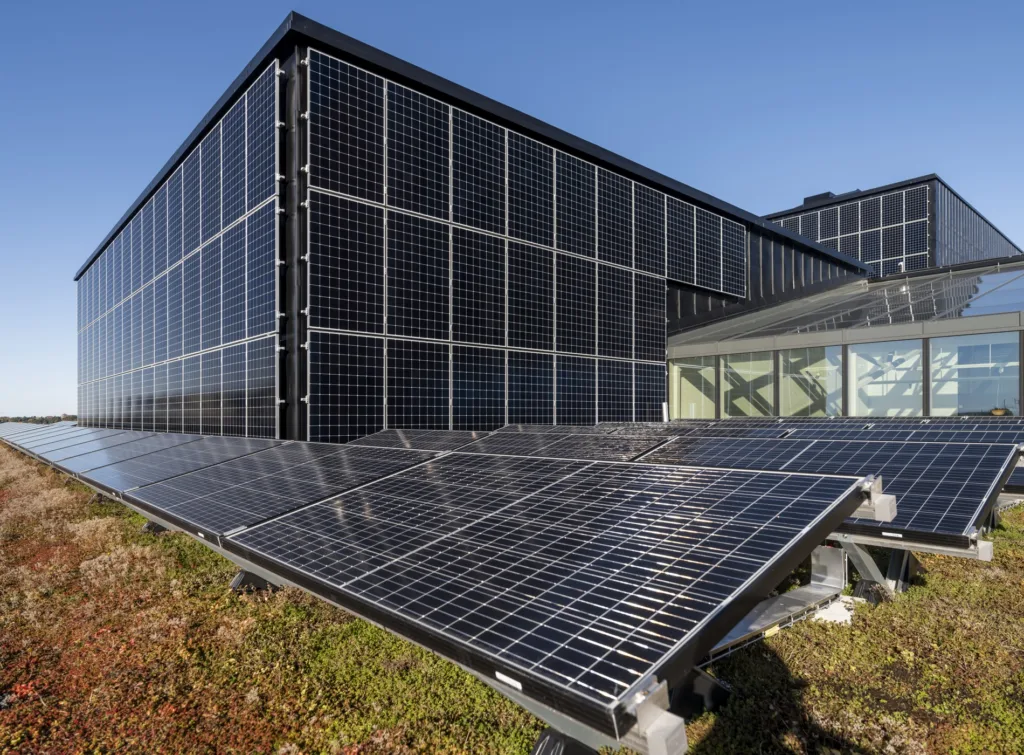 - Solpaneler monterade på tak och fasad av en modern byggnad, med klarblå himmel i bakgrunden.