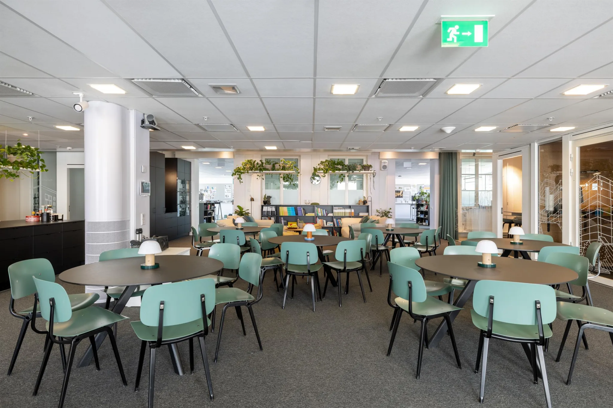 3. En matsal med flera runda bord och mintgröna stolar, inredd med växter och moderna belysningsdetaljer.